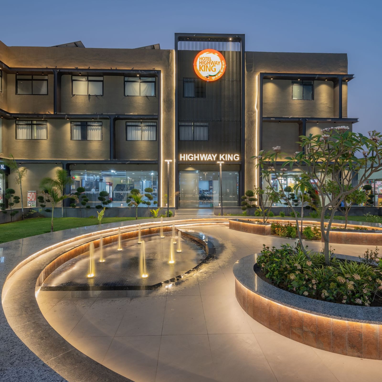 Facade and well-manicured lawn of Hotel Highway King, Behror, which also features a large illuminated logo of the property.