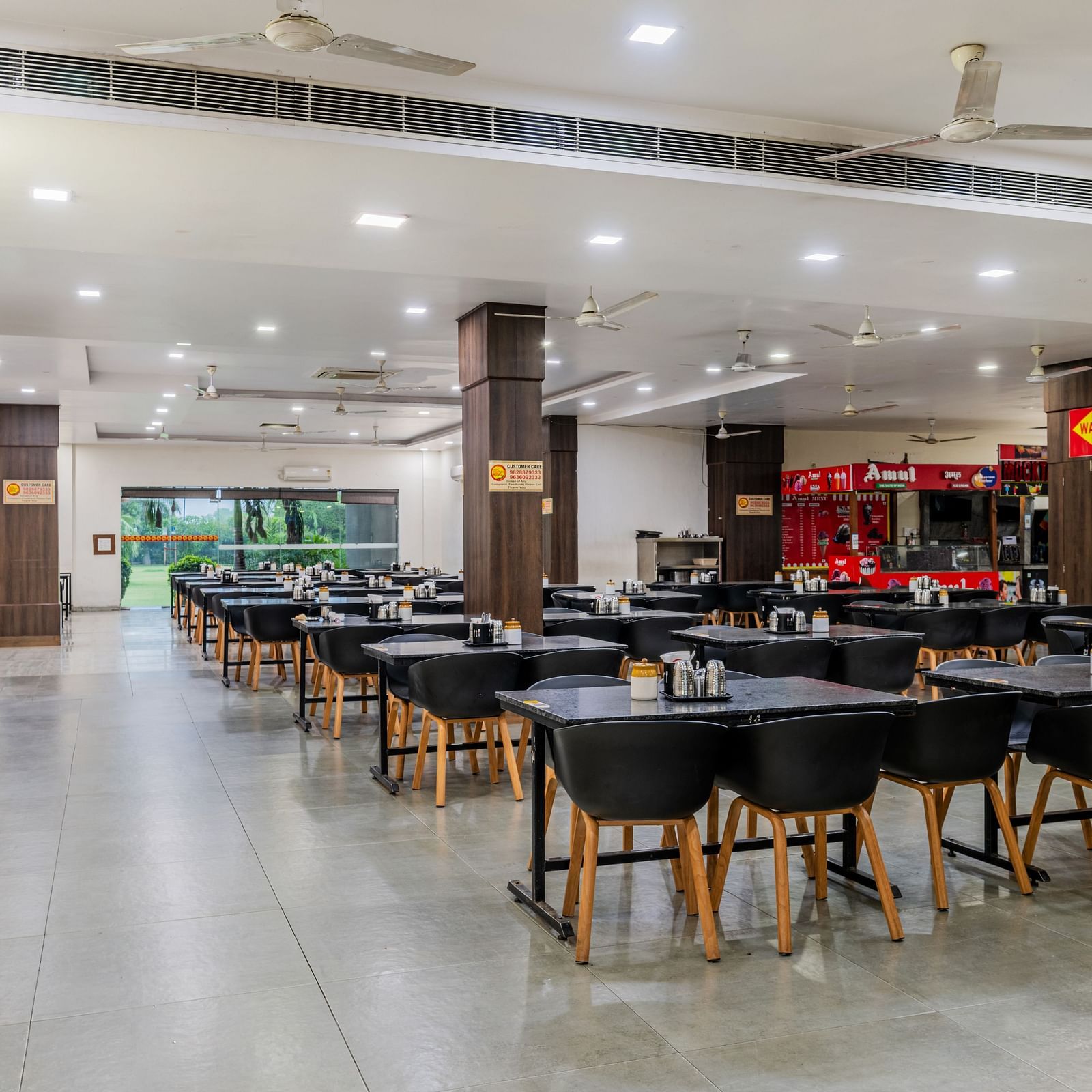 Dining tables with various seating capacities, ample lighting and eatery stalls located inside the restaurant of Hotel Highway King, Behror.