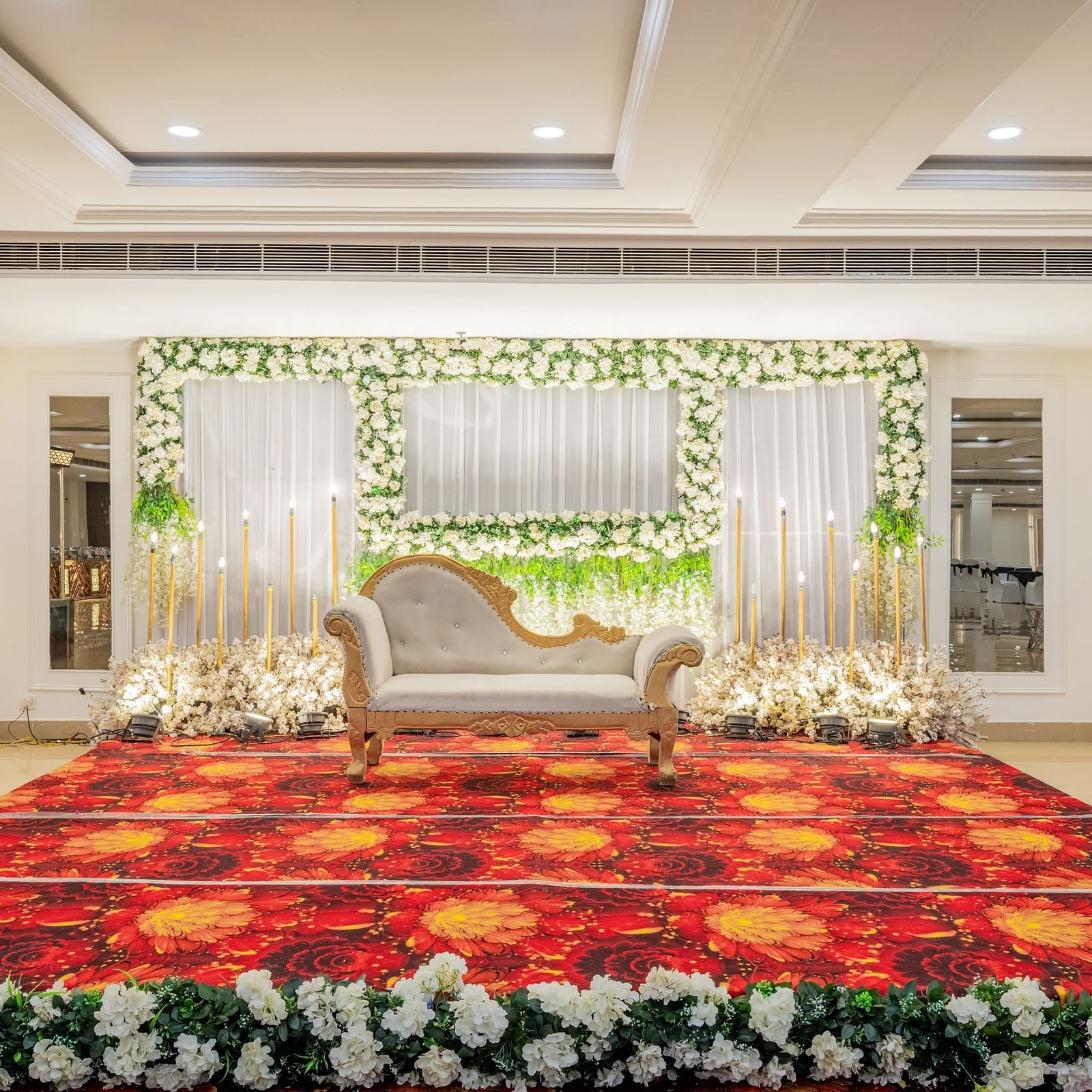 Indoor wedding stage setup with floral arrangements and red carpet at Hotel Highway King, Bilaspur.