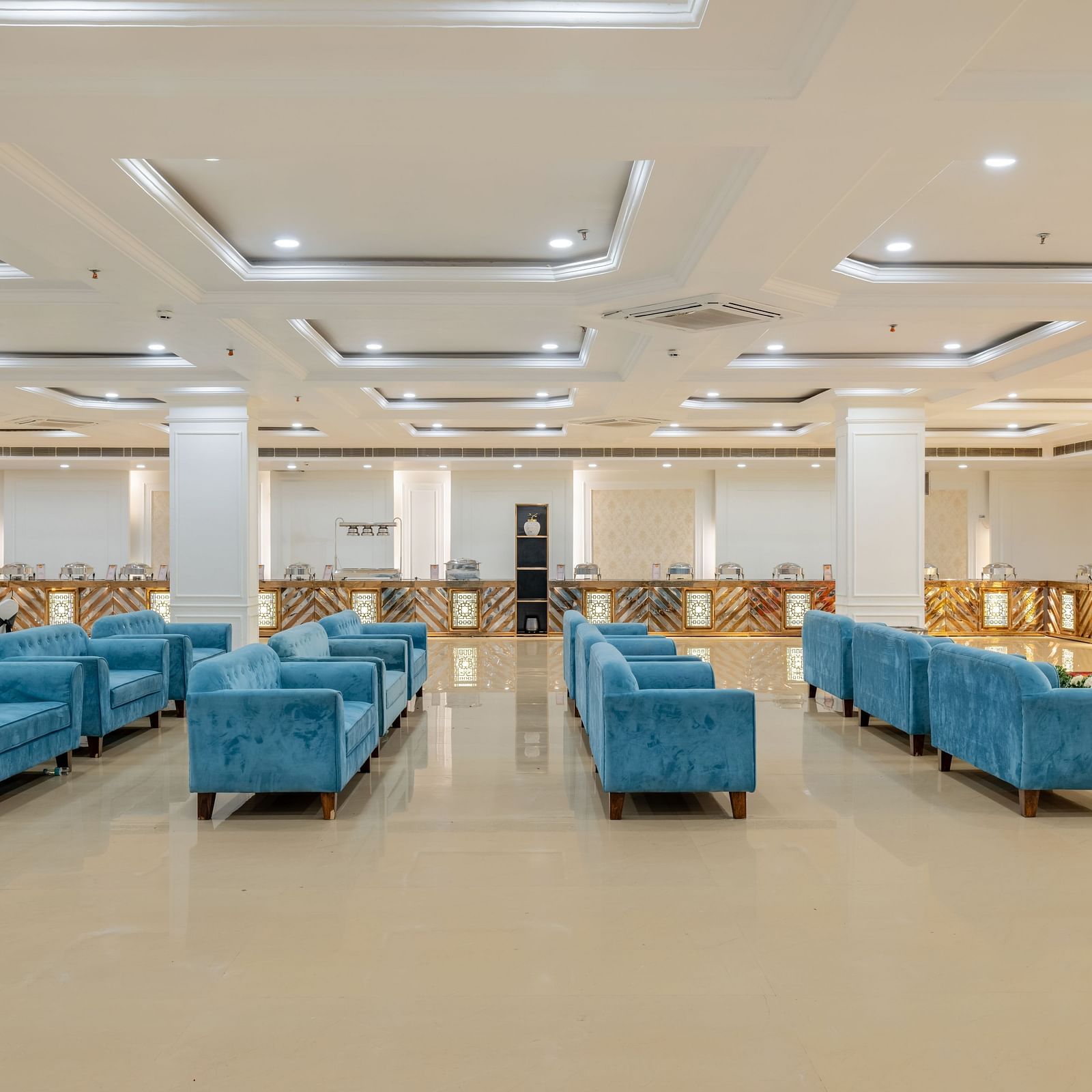 Spacious banquet hall with blue velvet seating and ambient ceiling lights at Hotel Highway King, Bilaspur.