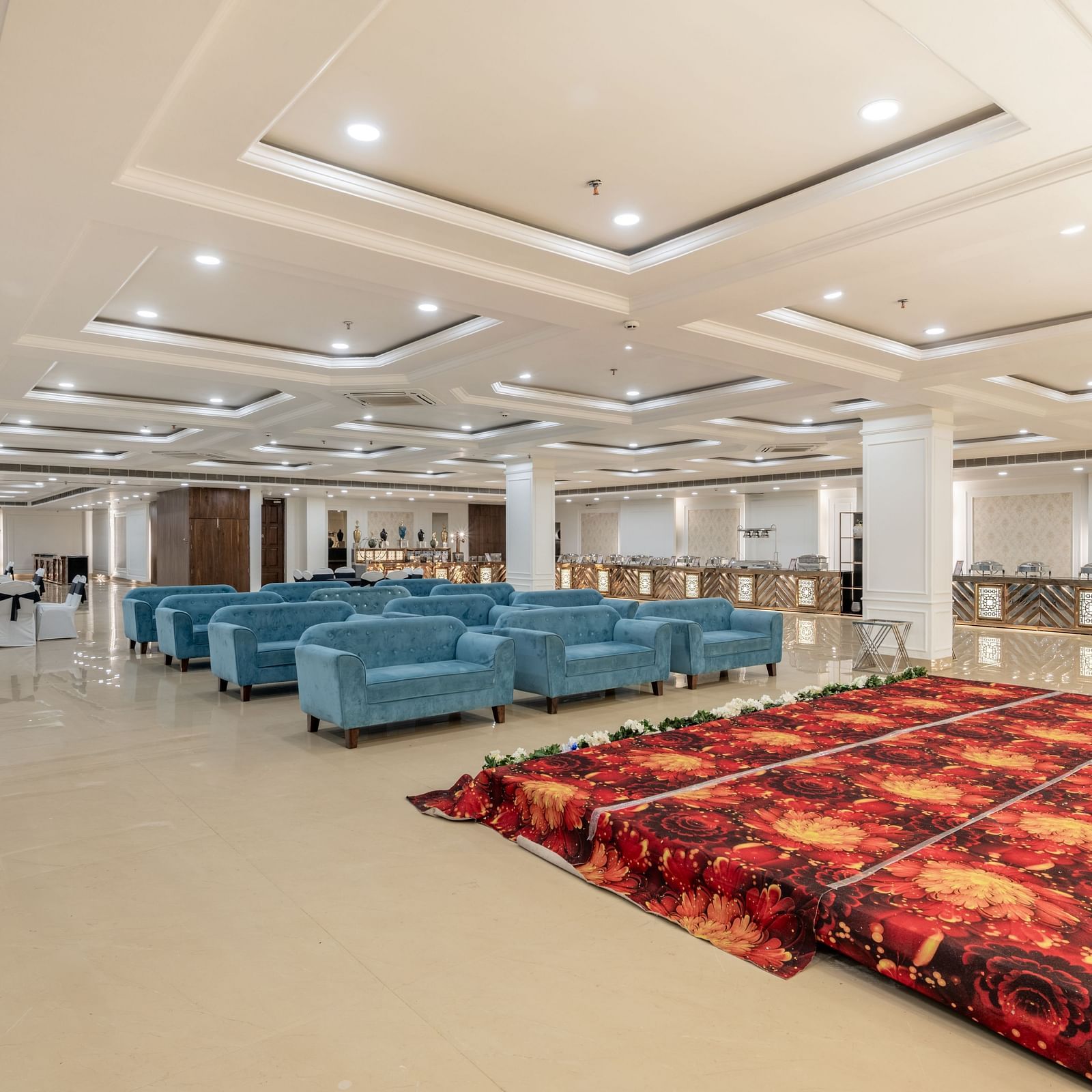 Versatile event hall with soft lighting, blue sofas, and red carpeted section at Hotel Highway King, Bilaspur.