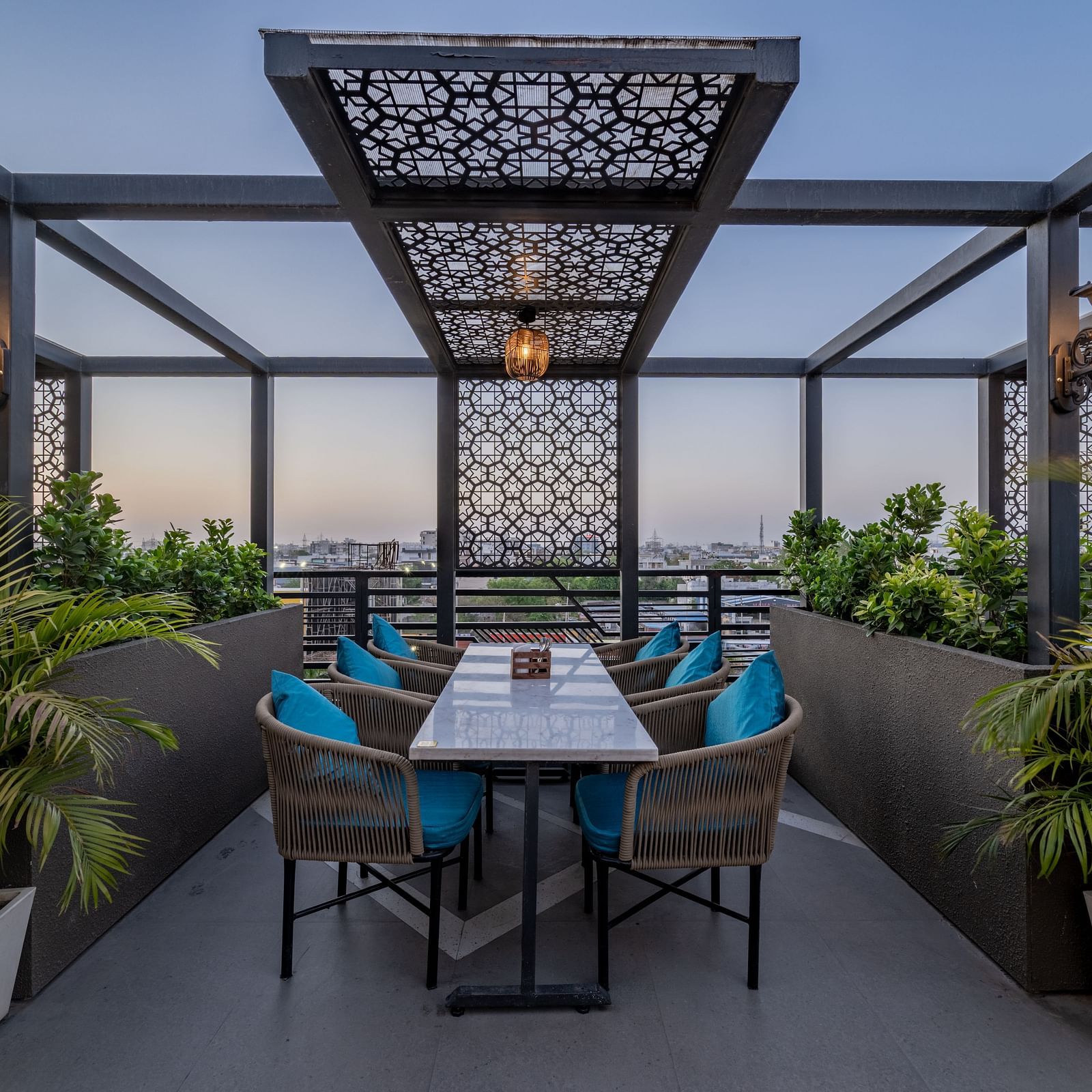Central rooftop dining set up under decorative latticework surrounded by greenery at Hotel Highway King, Jaipur.