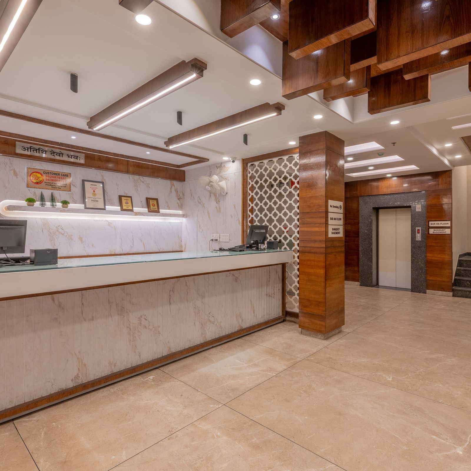 A view of the reception with white surfaces, wooden panels, and modern lighting at Hotel Highway King, Jaipur.