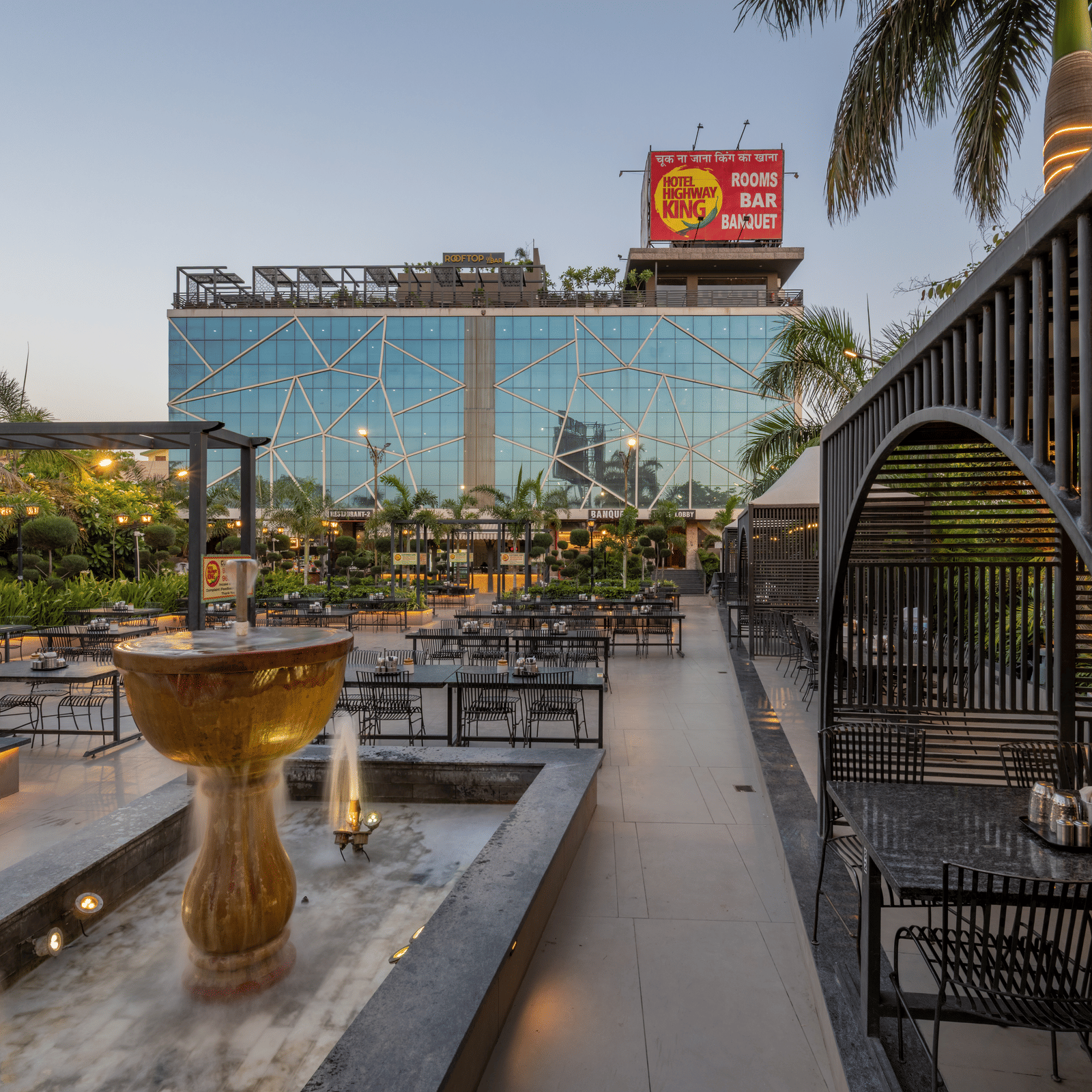 Rooftop view with central fountain, arched structure, and the facade of Hotel Highway King, Jaipur in background.