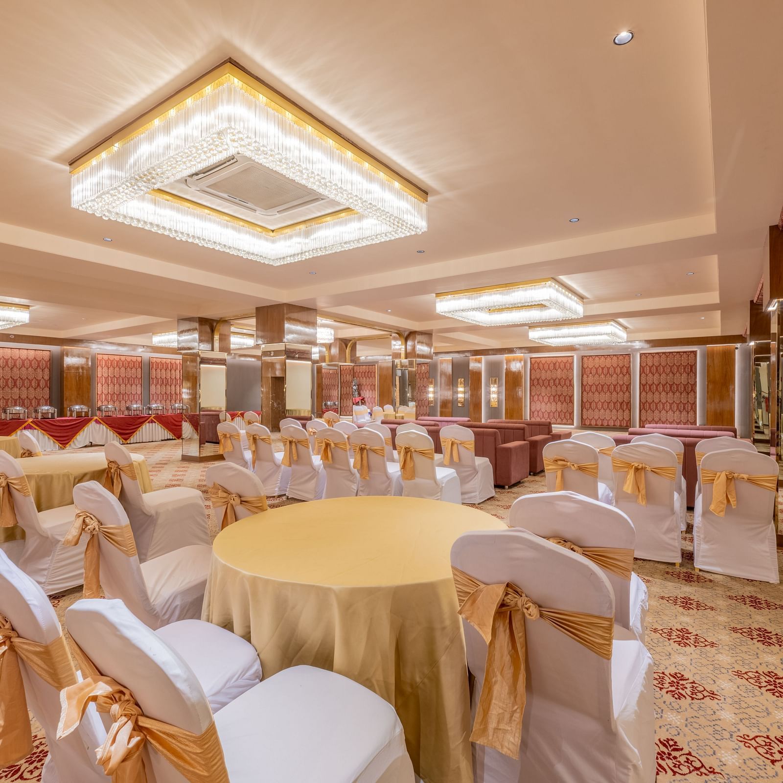Round tables with yellow tablecloths and white chairs arranged under a decorative ceiling light at Hotel Highway King, Jaipur.