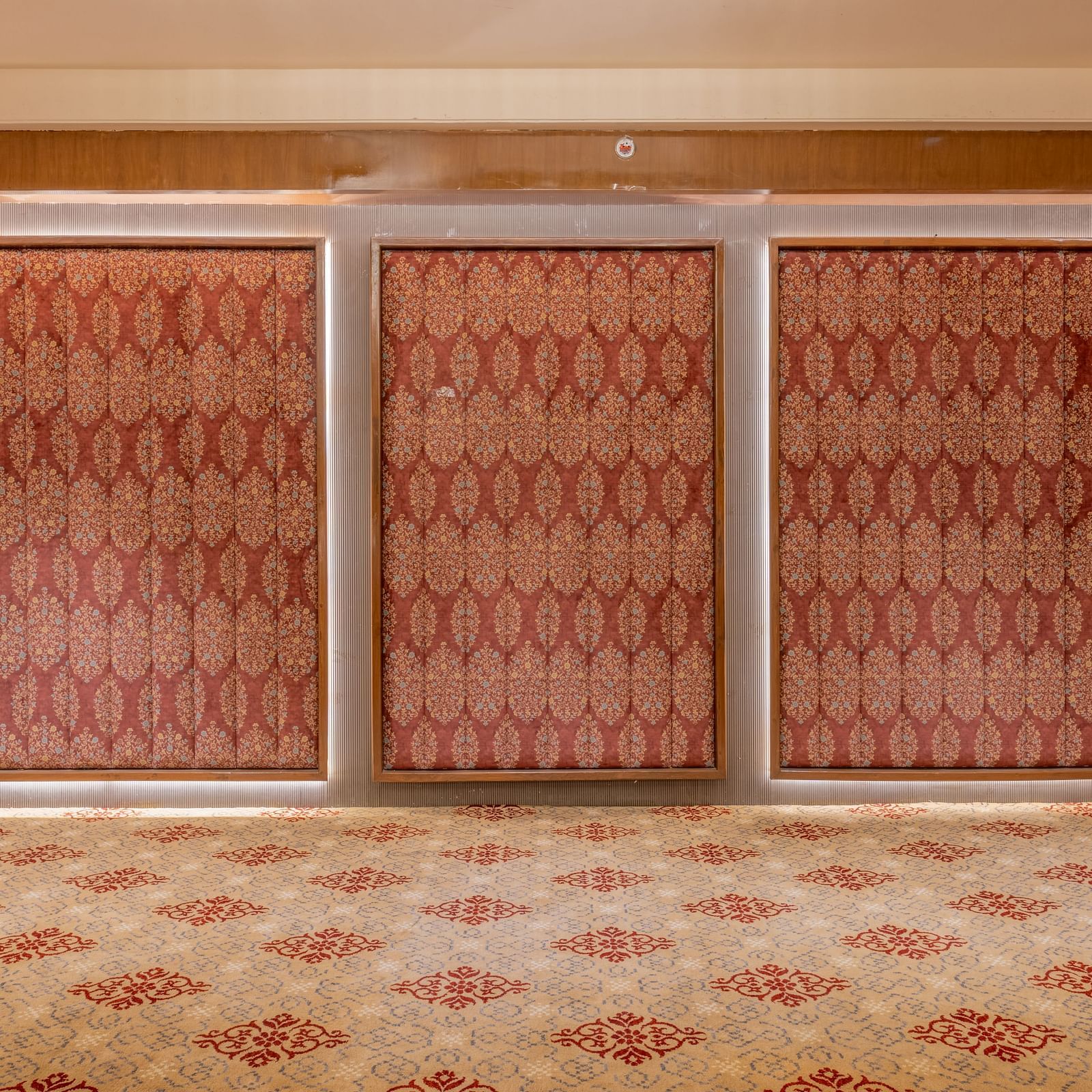 Closed banquet hall doors with patterned red panels and wooden framing on a carpeted floor at Hotel Highway King, Jaipur.