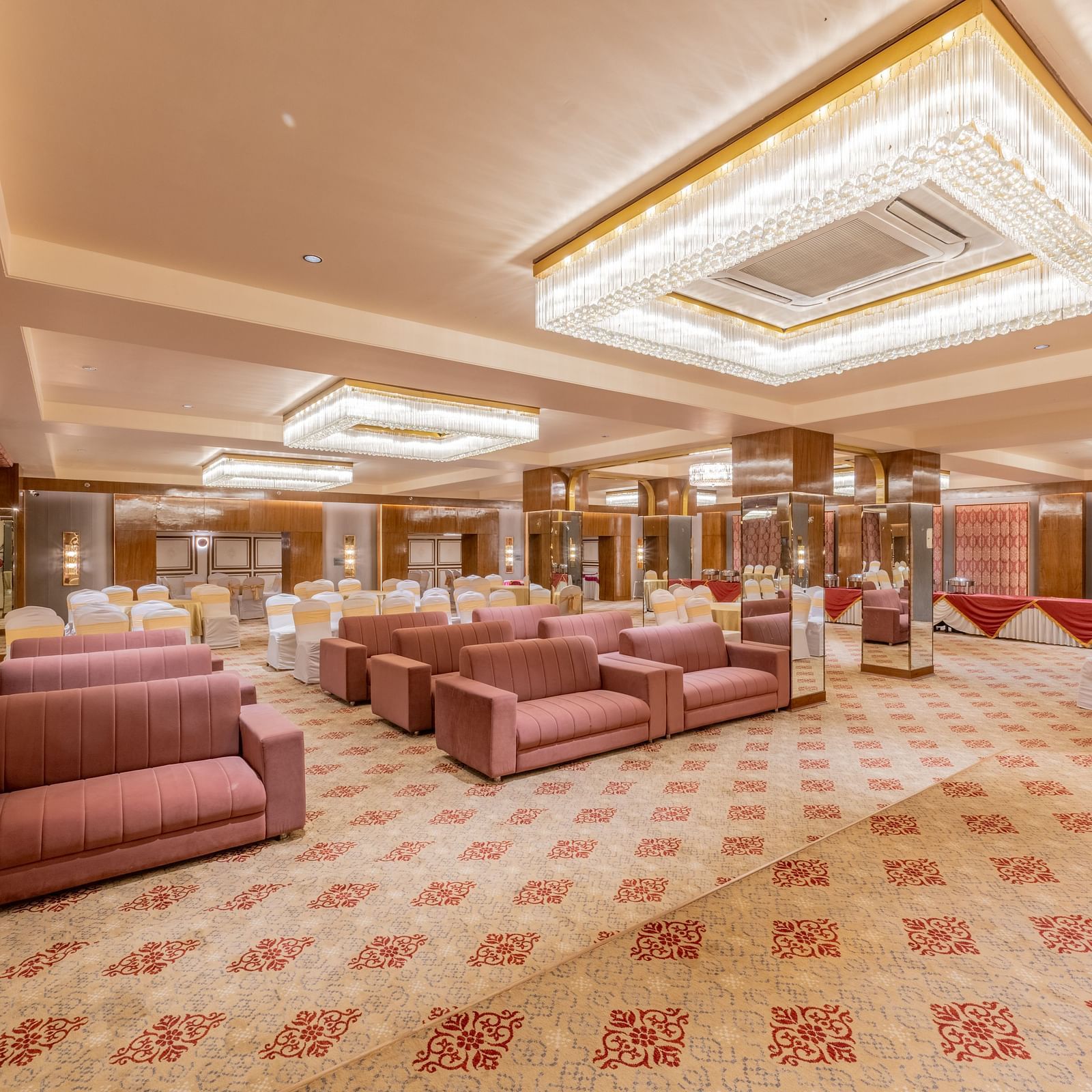 Large banquet hall with maroon sofas, chandeliers, and patterned carpet at Hotel Highway King, Jaipur.
