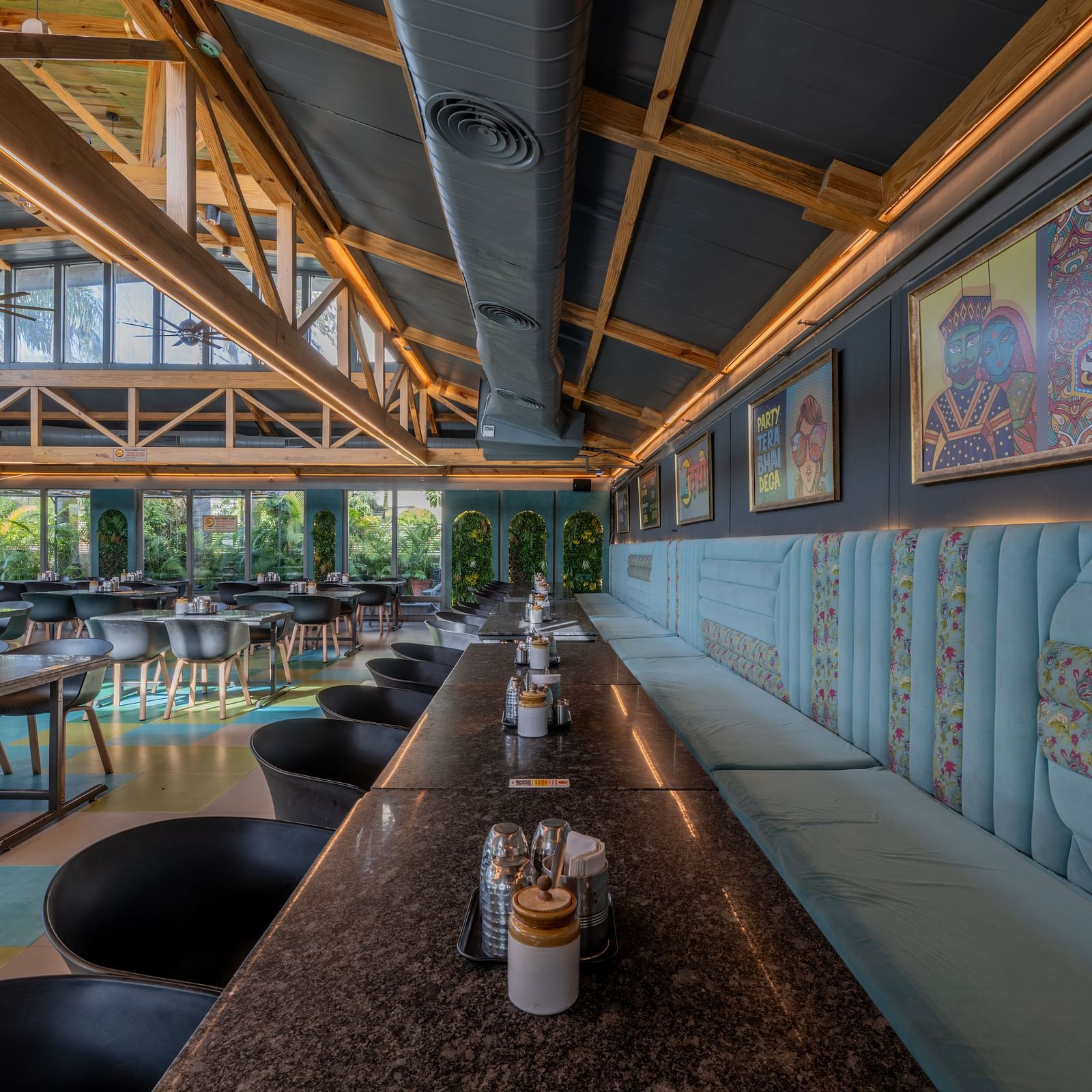 Long table seating next to artwork and blue panelling under wooden rafters at Hotel Highway King, Jaipur.