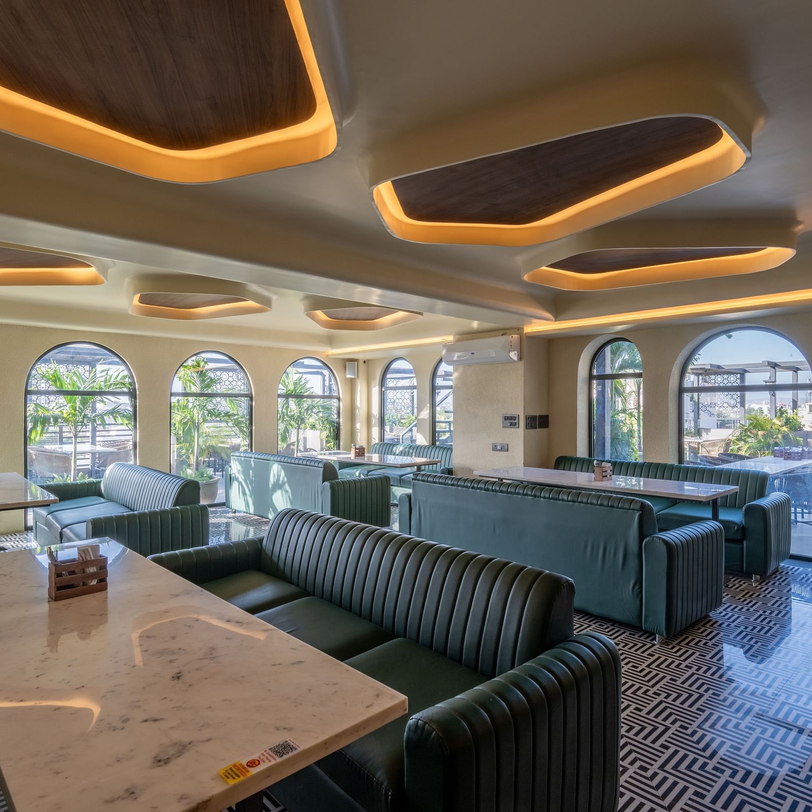 Lounge dining space with marble tables, green seating, and arched glass windows at Hotel Highway King, Jaipur.