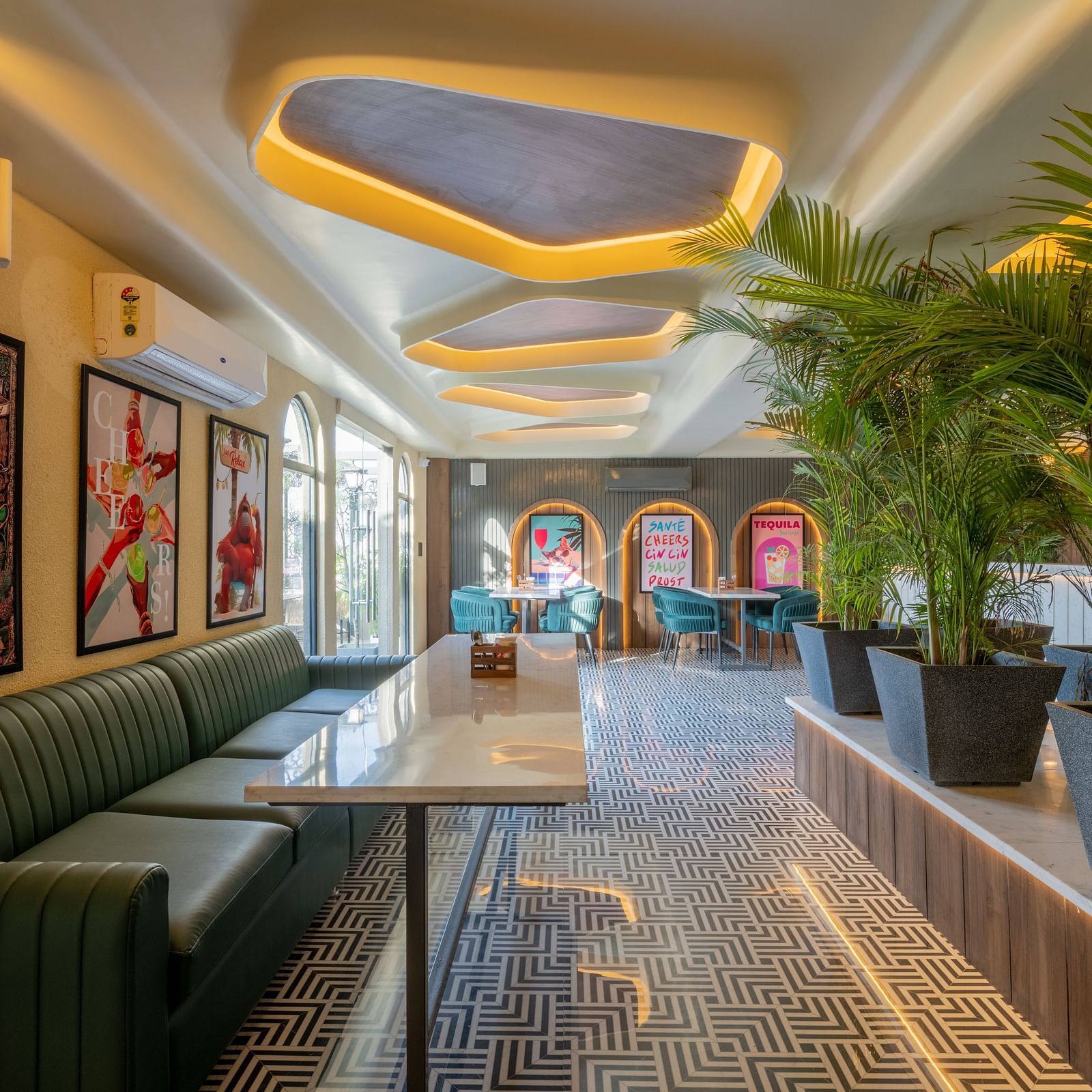 Cosy lounge corner with green seating, framed posters, plants, and ceiling lights at Hotel Highway King, Jaipur.
