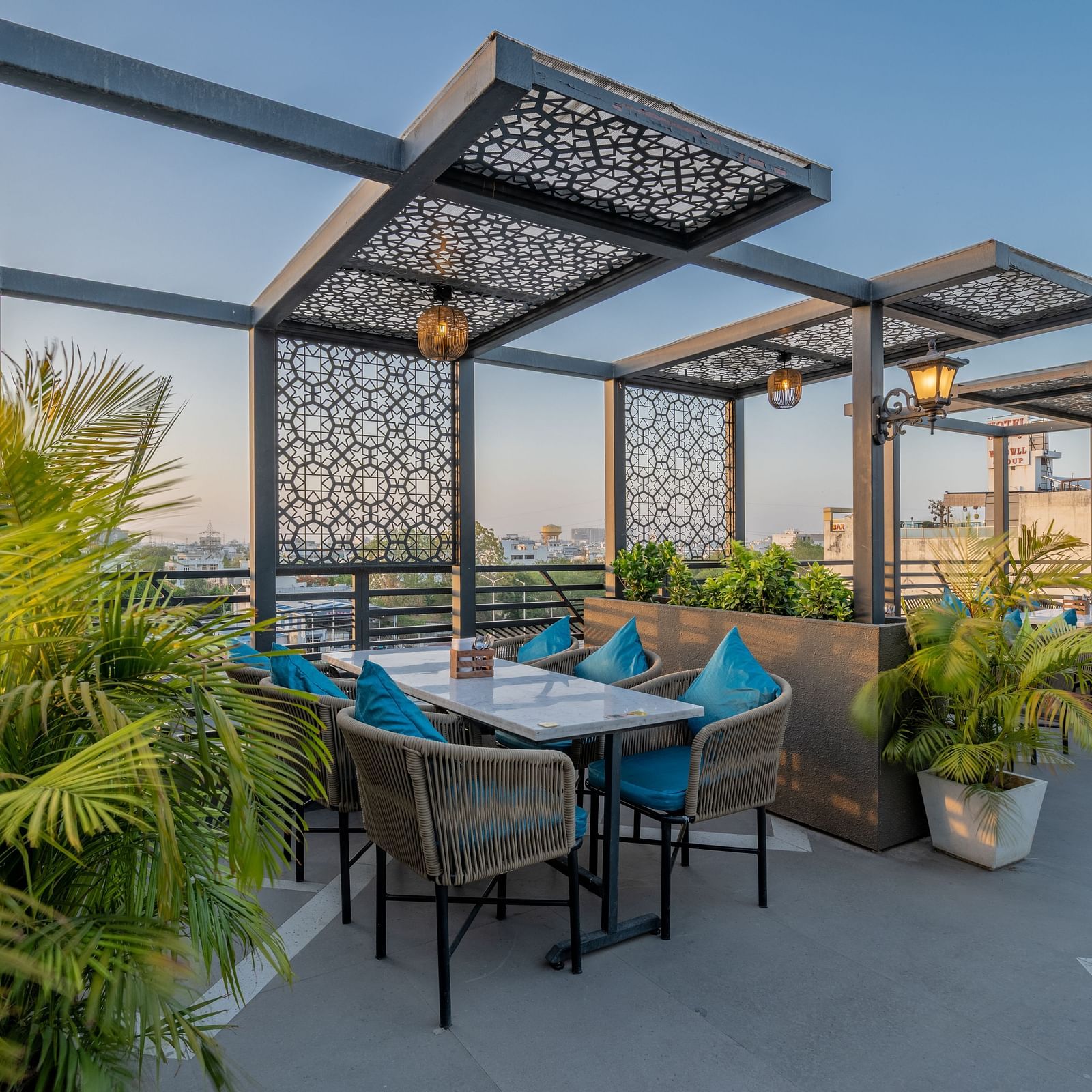Pergola-covered rooftop dining space with blue cushions and lantern-style lighting at Hotel Highway King, Jaipur.