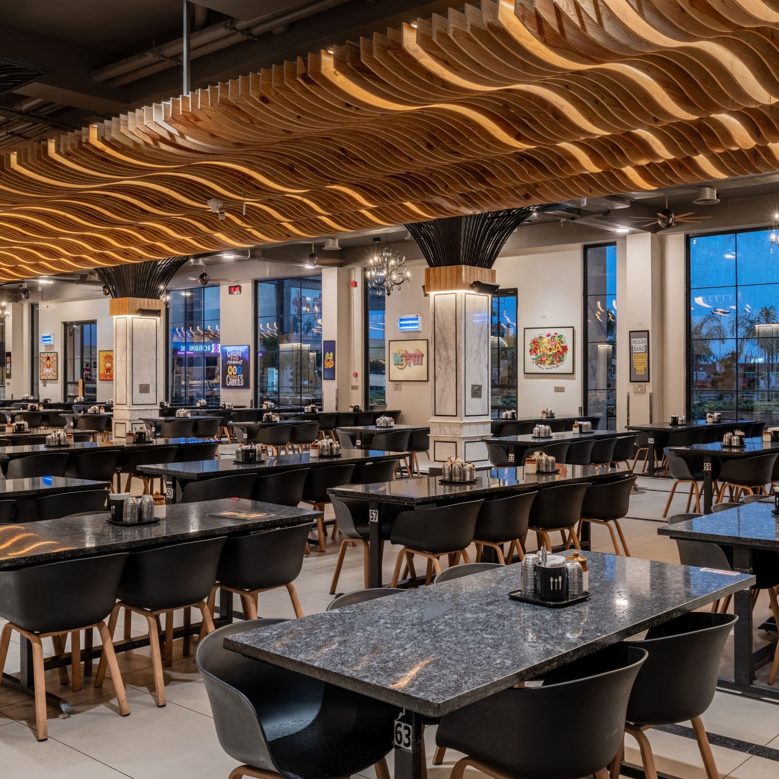 The spacious dining area at Hotel Highway King, Kishangarh, features modern tables and chairs under a wavy ceiling design.