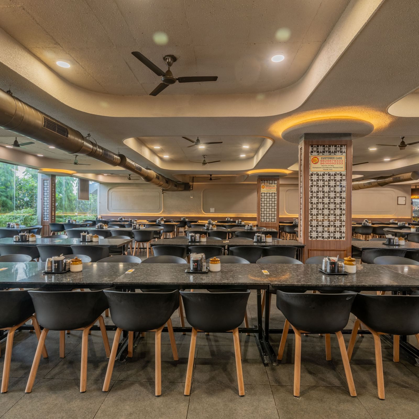 Chairs neatly arranged around a table with a glass panel to the side, offering a view of the lawn at Hotel Highway King, Neelka.