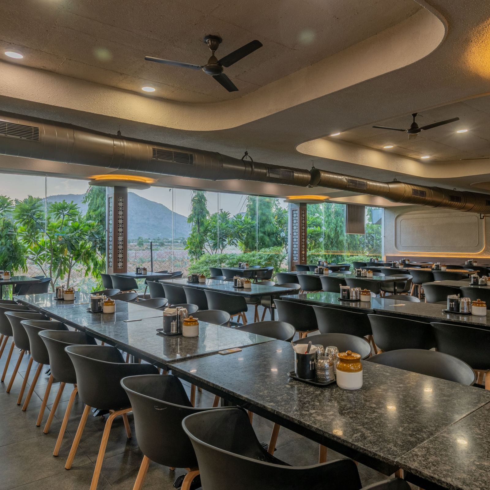 Spacious, modern dining area with black chairs, large windows, and ambient lighting at Hotel Highway King, Neelka.