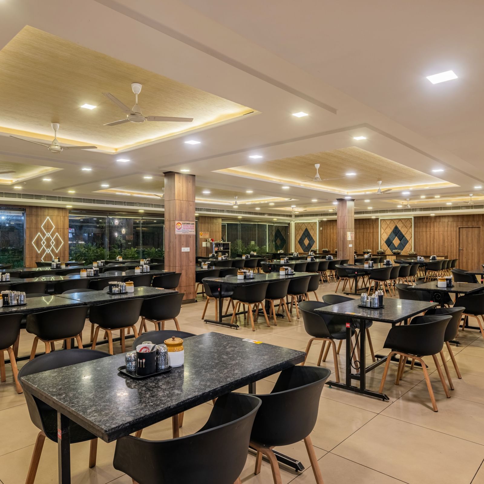An empty, well-lit dining area inside the Hotel Highway King Shahpura, set with numerous tables and chairs.