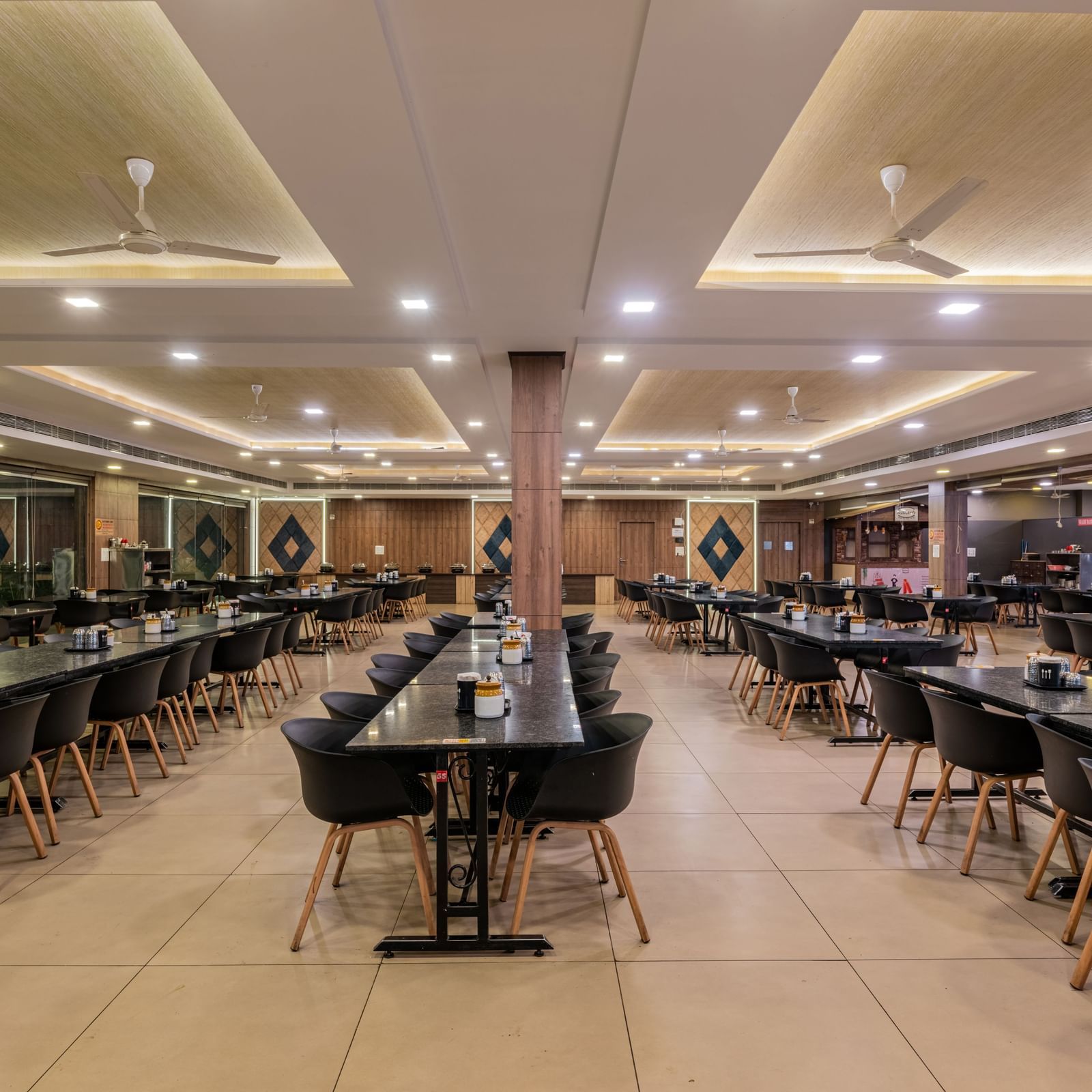 A bright and expansive dining hall with numerous tables and black chairs, ready for guests at Hotel Highway King Shahpura.