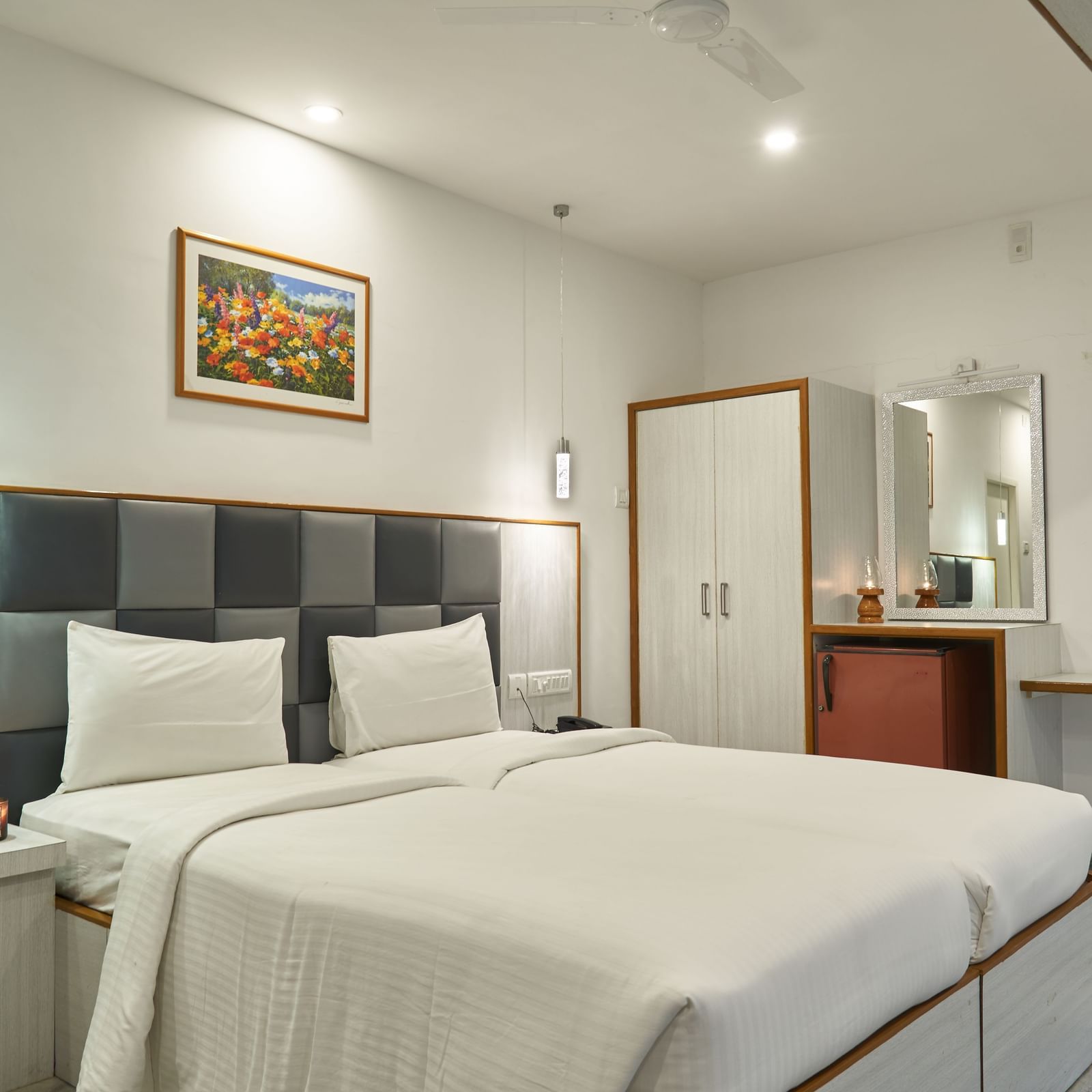 A comfortable and well-appointed hotel room at Hotel Mamallaa Heritage, featuring a large bed with crisp white linens, a bedside table, and wall-mounted art.