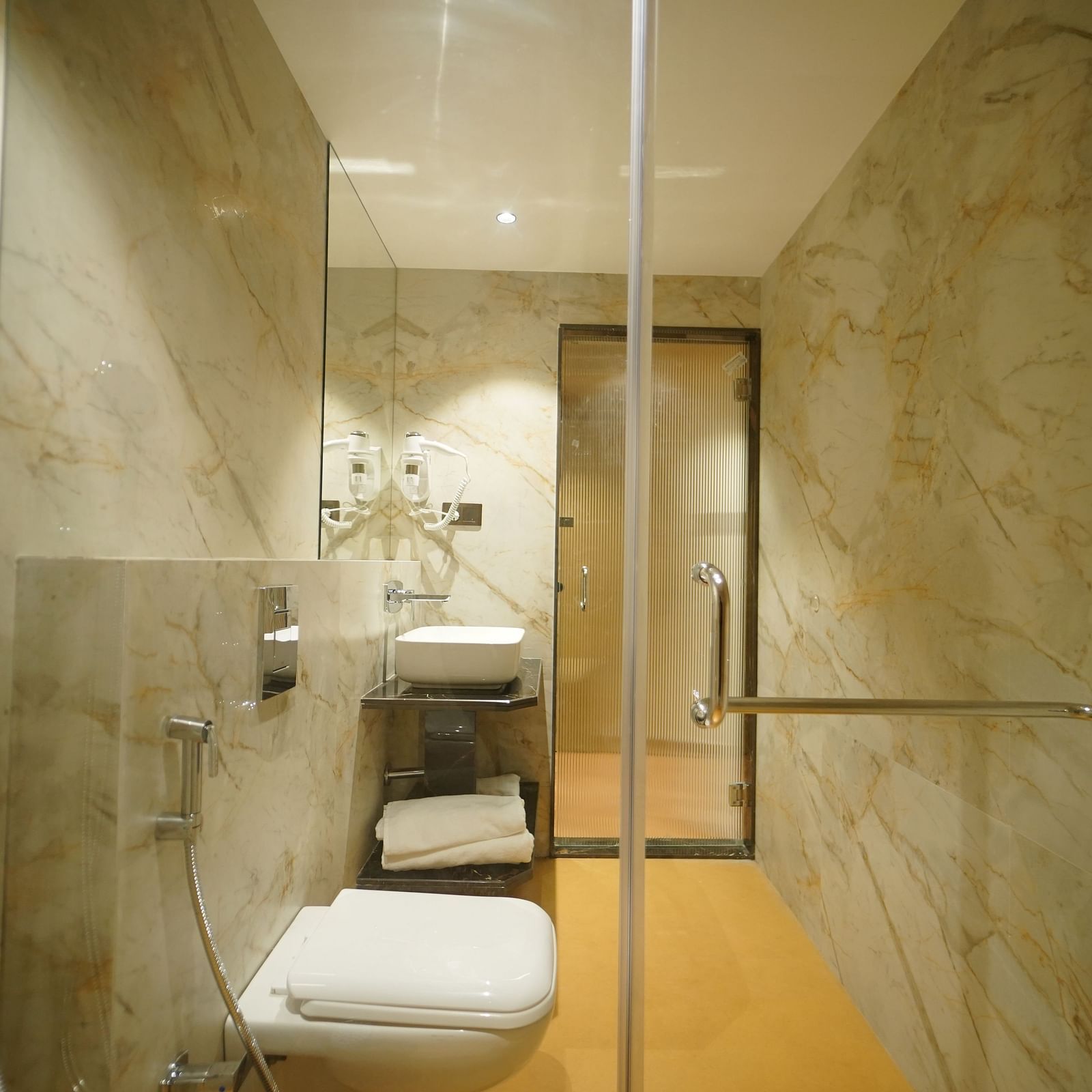 A modern bathroom features a toilet, a shower with glass enclosure and fixtures, and a glimpse of a sink area - Hotel Park Inn, Nellore.