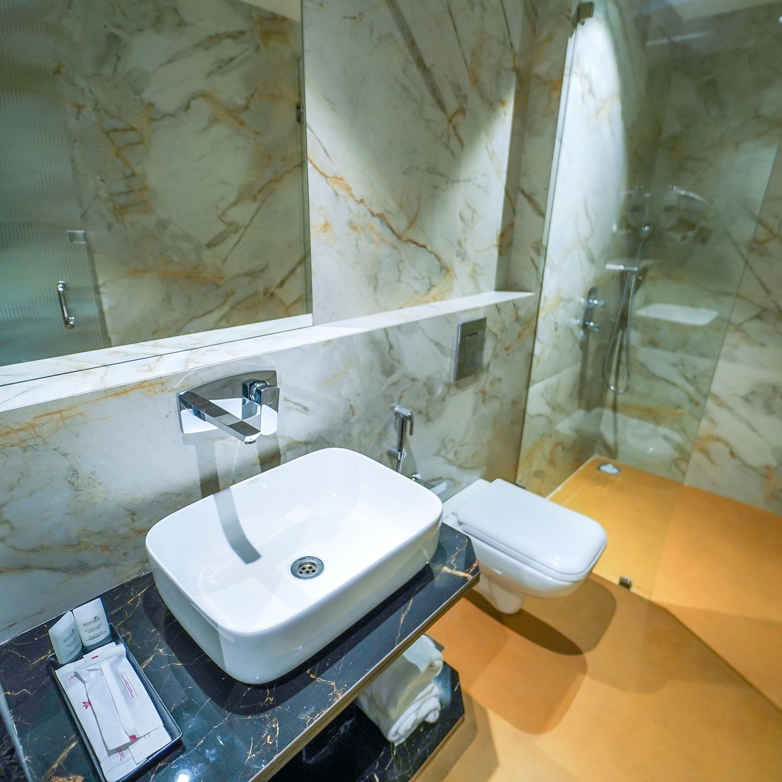 A bathroom includes a sink with a modern faucet, a mirror, a toilet, and a shower area with fixtures - Hotel Park Inn, Nellore.