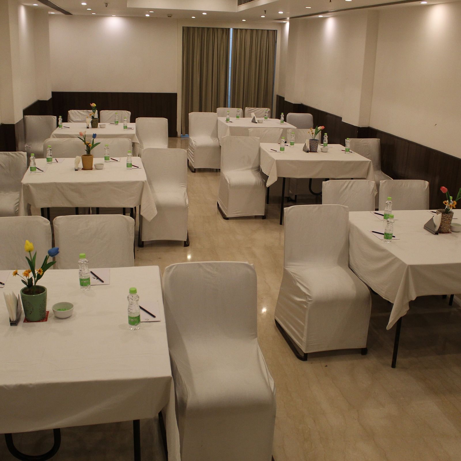 An image of a banquet hall at Inde Hotel Vista Woods featuring a few sets of tables with four chairs each