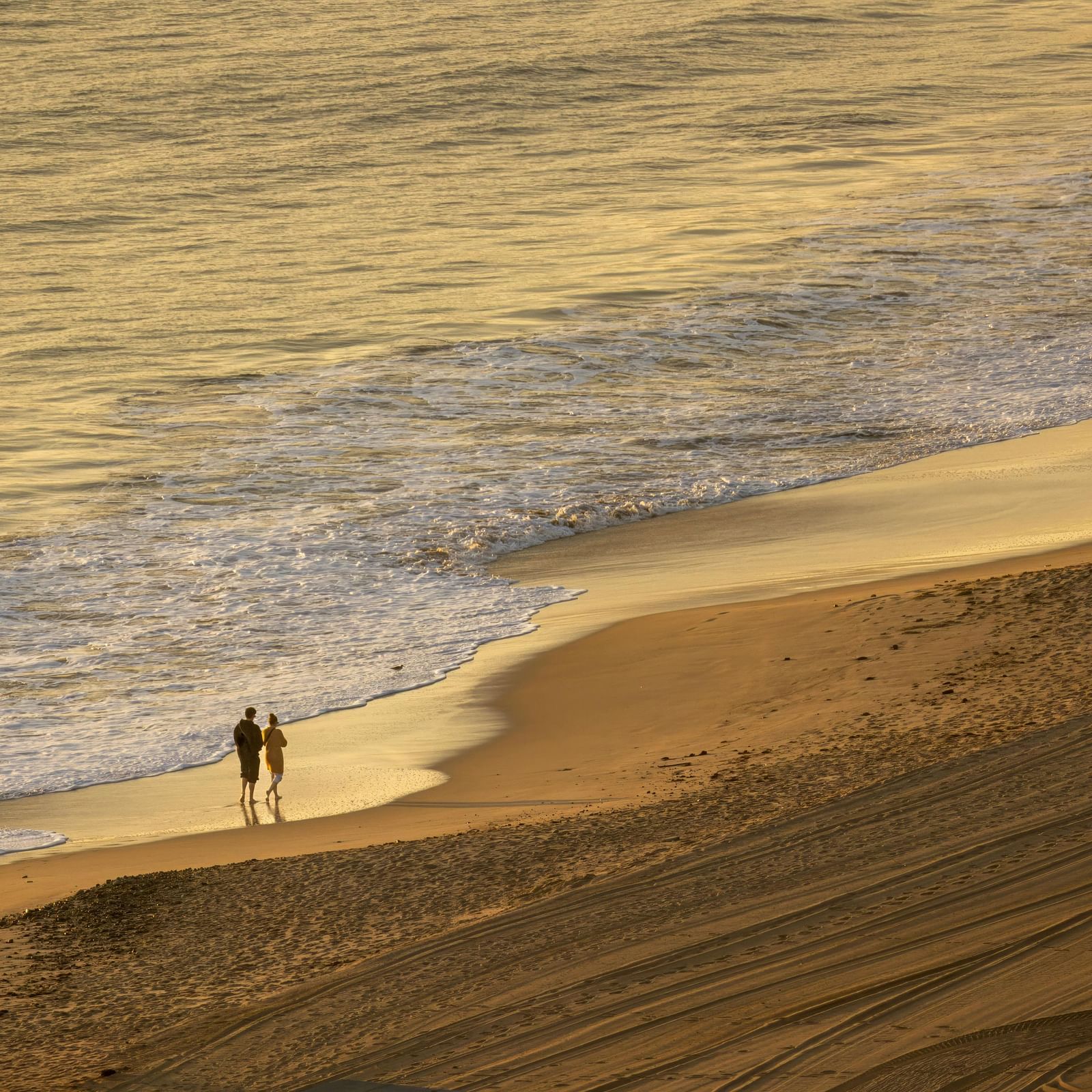 A far-angle view of a couple walking on the beach during sunset.