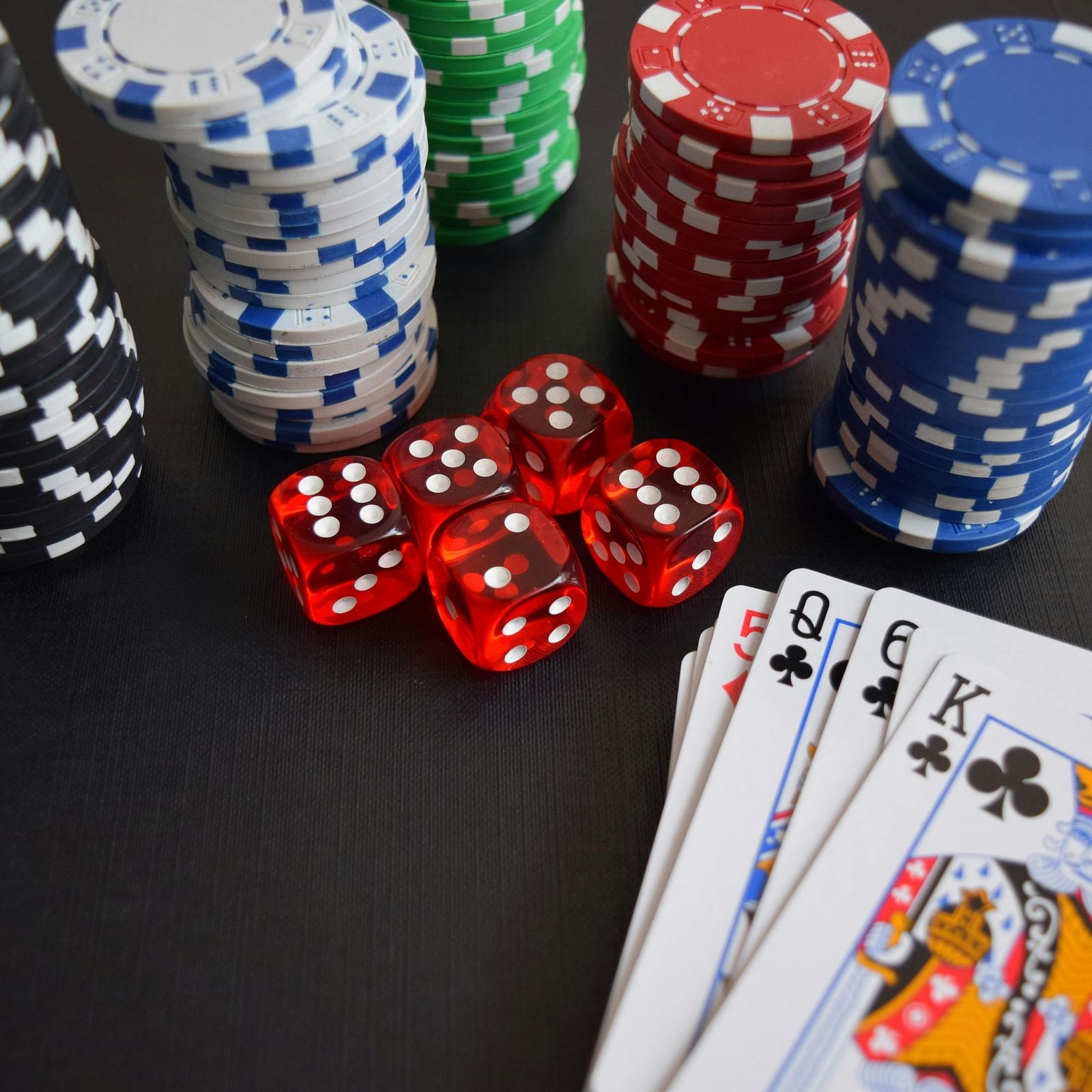 Playing cards placed next to poker chips and dices on a wooden surface.