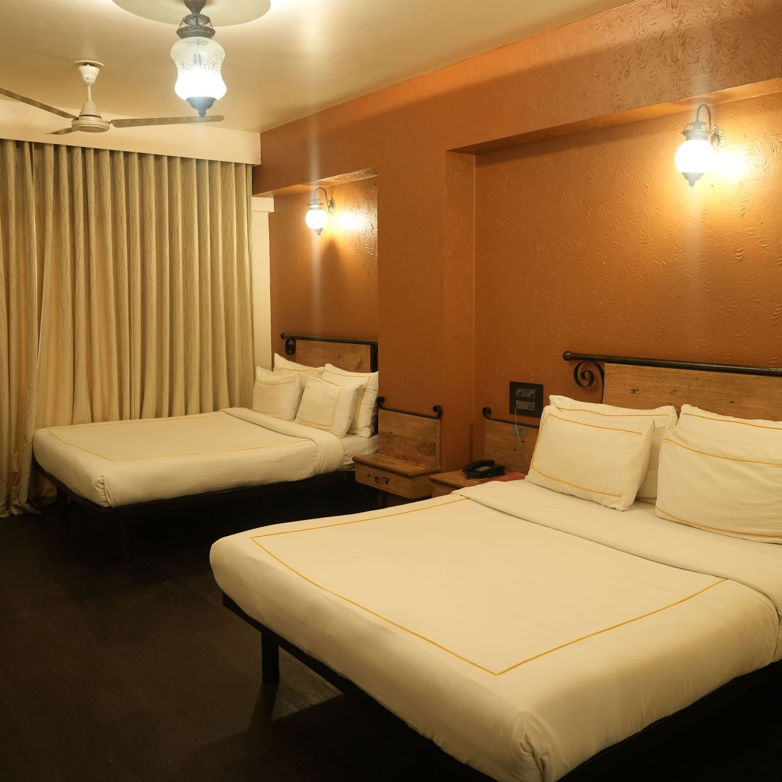 Bedroom with two double beds, curtains and warm lighting at Infiniti Hotel, Indore.