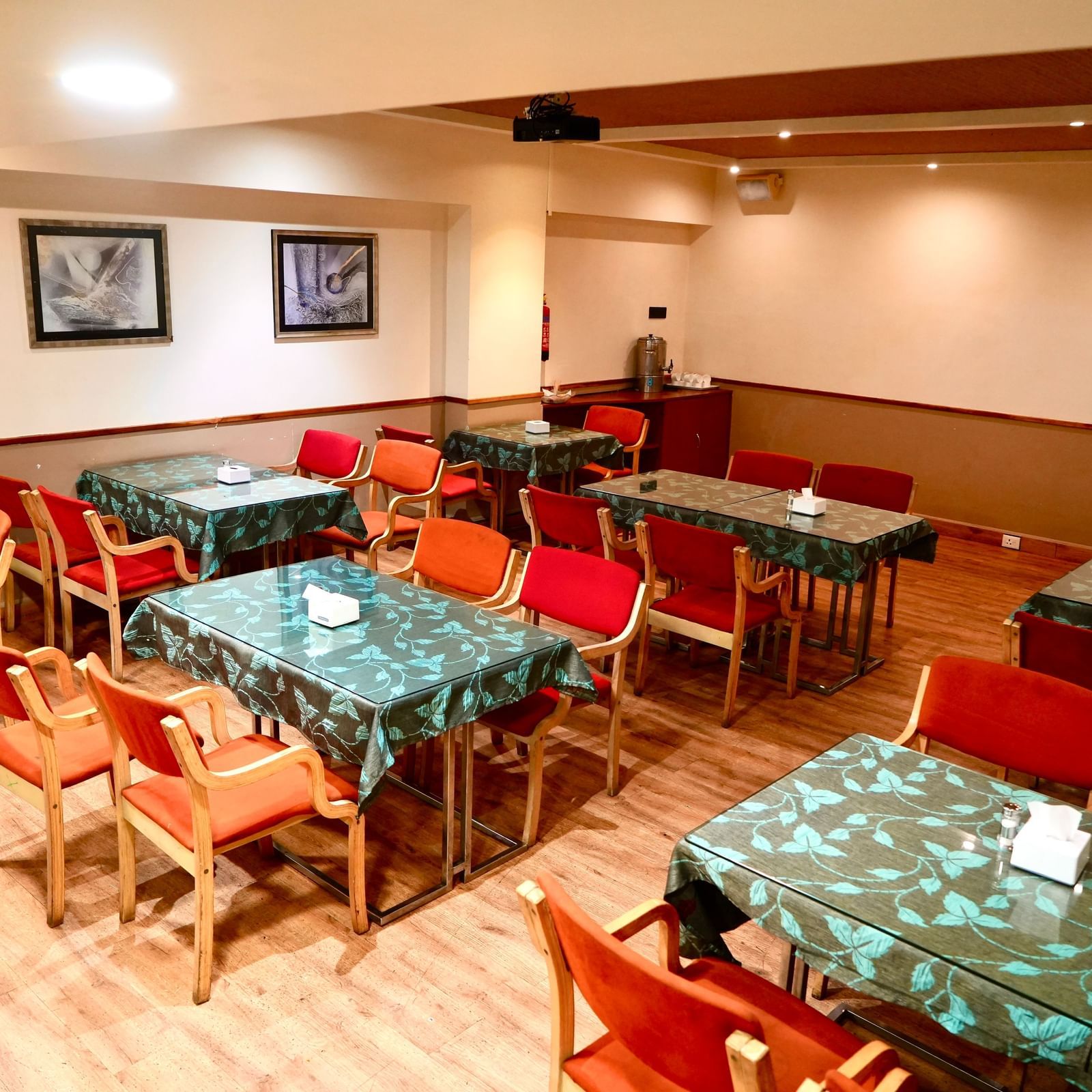 An empty dining room with multiple tables, patterned tablecloths, and several upholstered chairs at Infiniti Hotel, Indore.