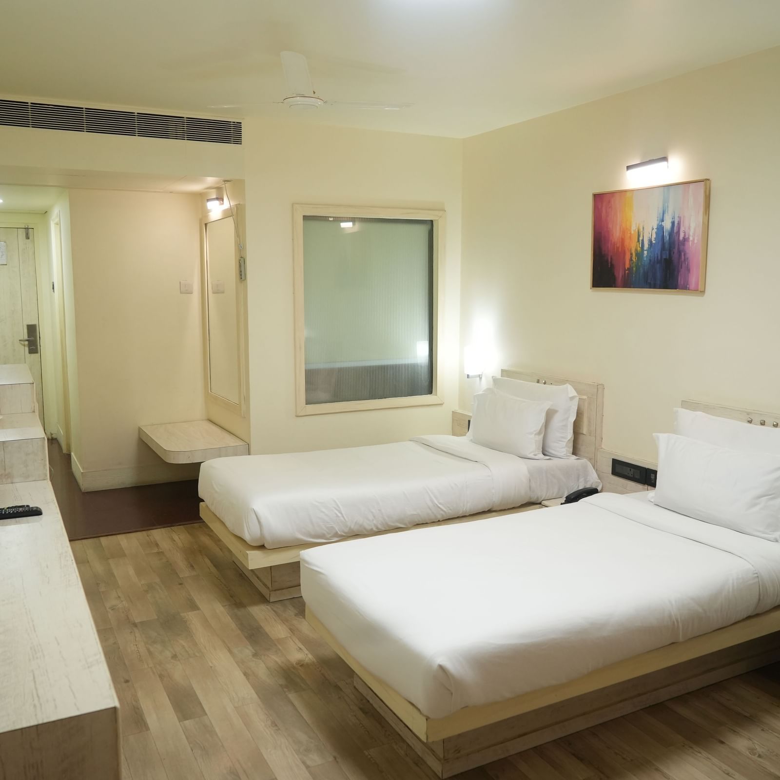 Bedroom with 2 single beds, a television, desk and wall paintings at Infiniti Hotel, Indore.