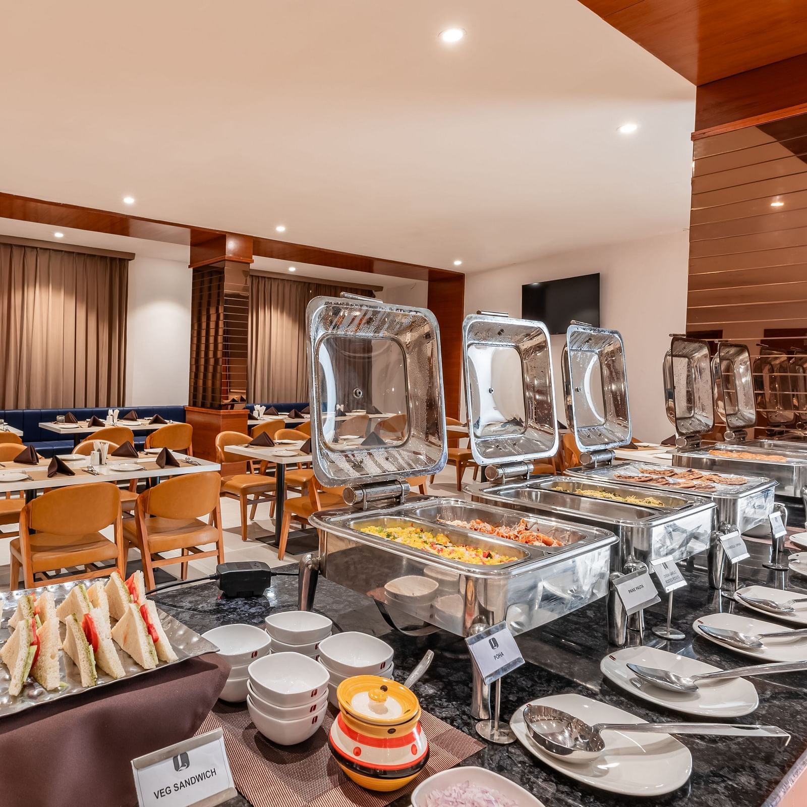 A buffet spread with covered food warmers, plates, and other serving dishes is ready in a dining area - Lords Eco Inn Ambaji.