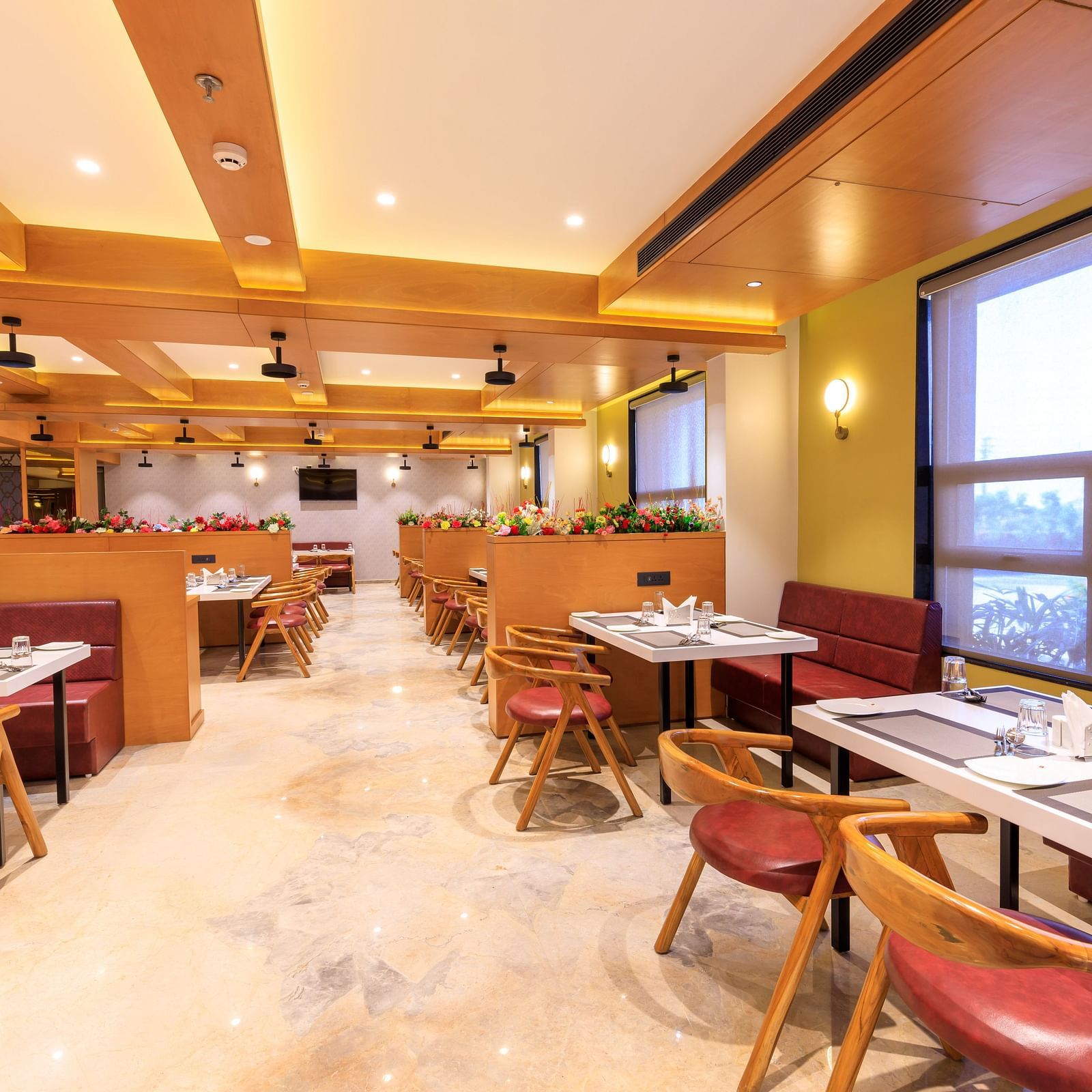 The brightly lit restaurant at Lords Eco Inn Apple Gate features set tables, red chairs, wooden accents, and natural light from large windows.