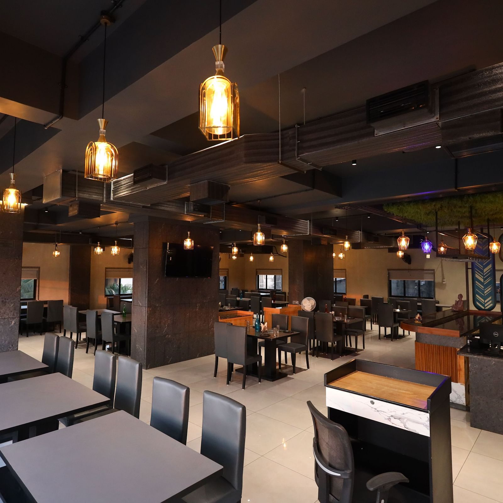 The image shows a restaurant interior with tables, chairs, booth seating, a service counter, and warm pendant lighting - Lords Eco Inn Navsari.