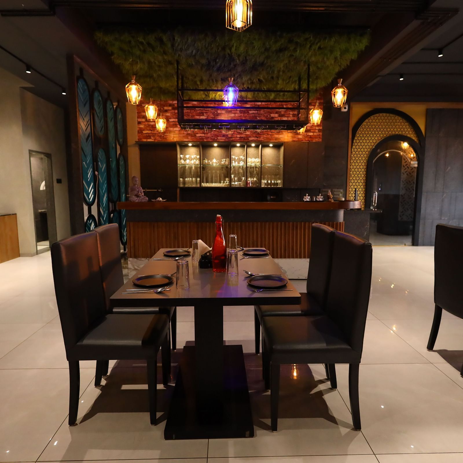 The image shows a restaurant dining area with set tables and chairs, a bar in the background, and warm lighting - Lords Eco Inn Navsari.
