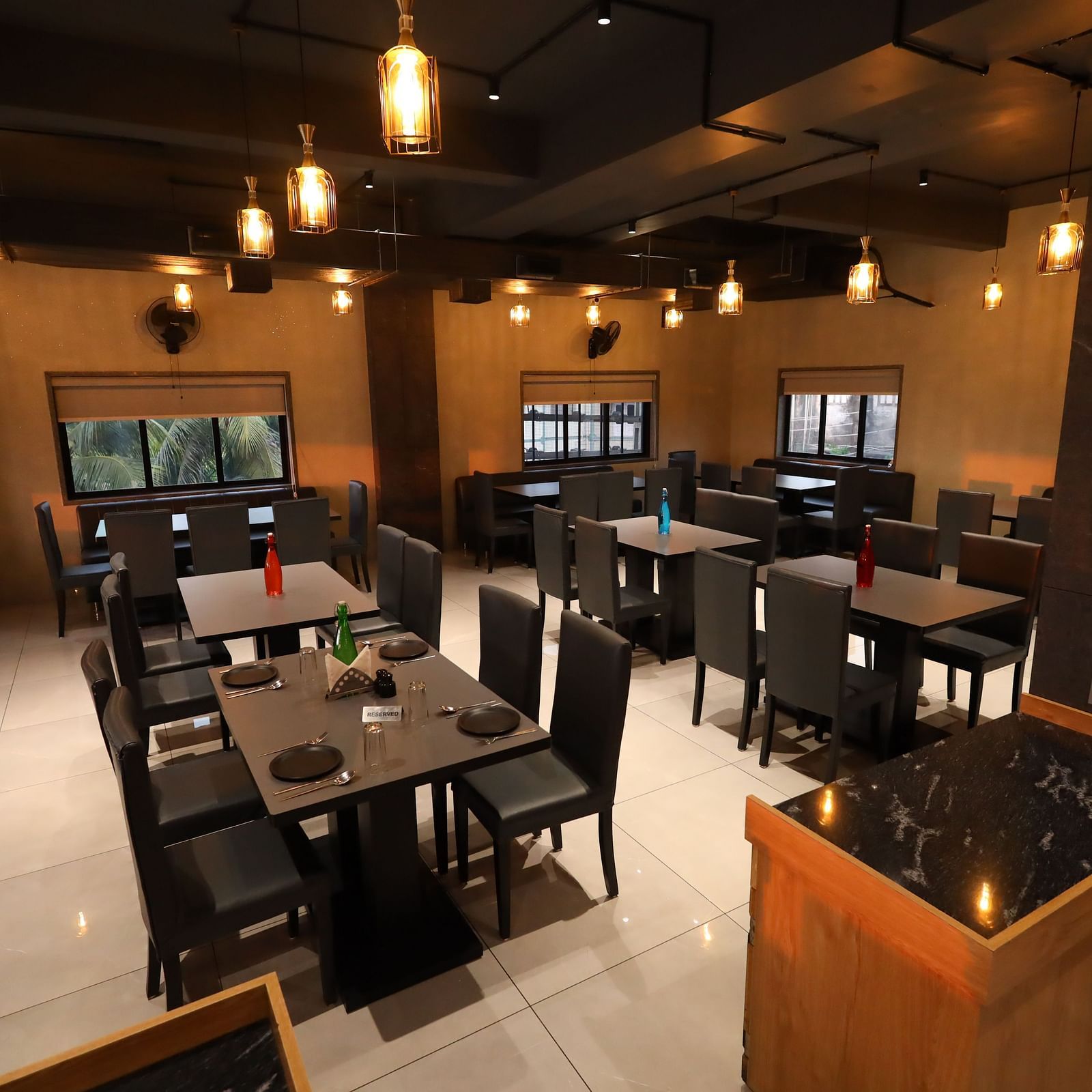 The image depicts a restaurant interior with set tables and chairs under warm, hanging lights - Lords Eco Inn Navsari.