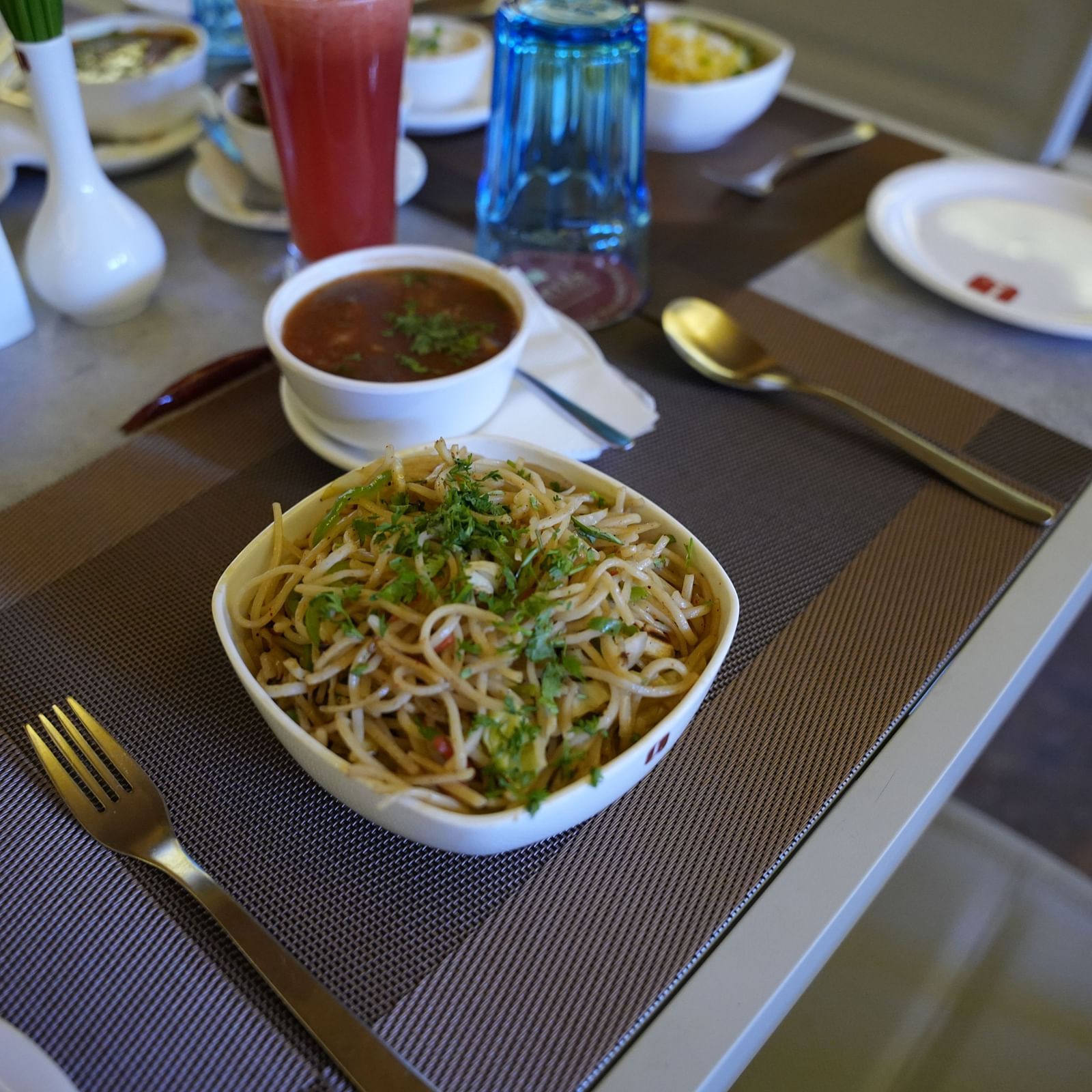 a bowl of noodles and soup kept in between steel cutleries on a dining table