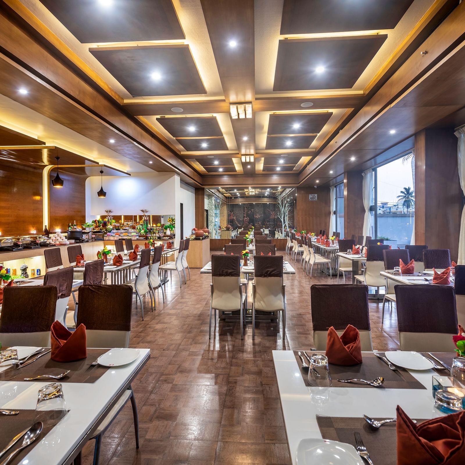 A spacious and elegantly designed restaurant with well-set tables adorned with flowers and large windows offering a view of the outdoors at Lords Inn Somnath.