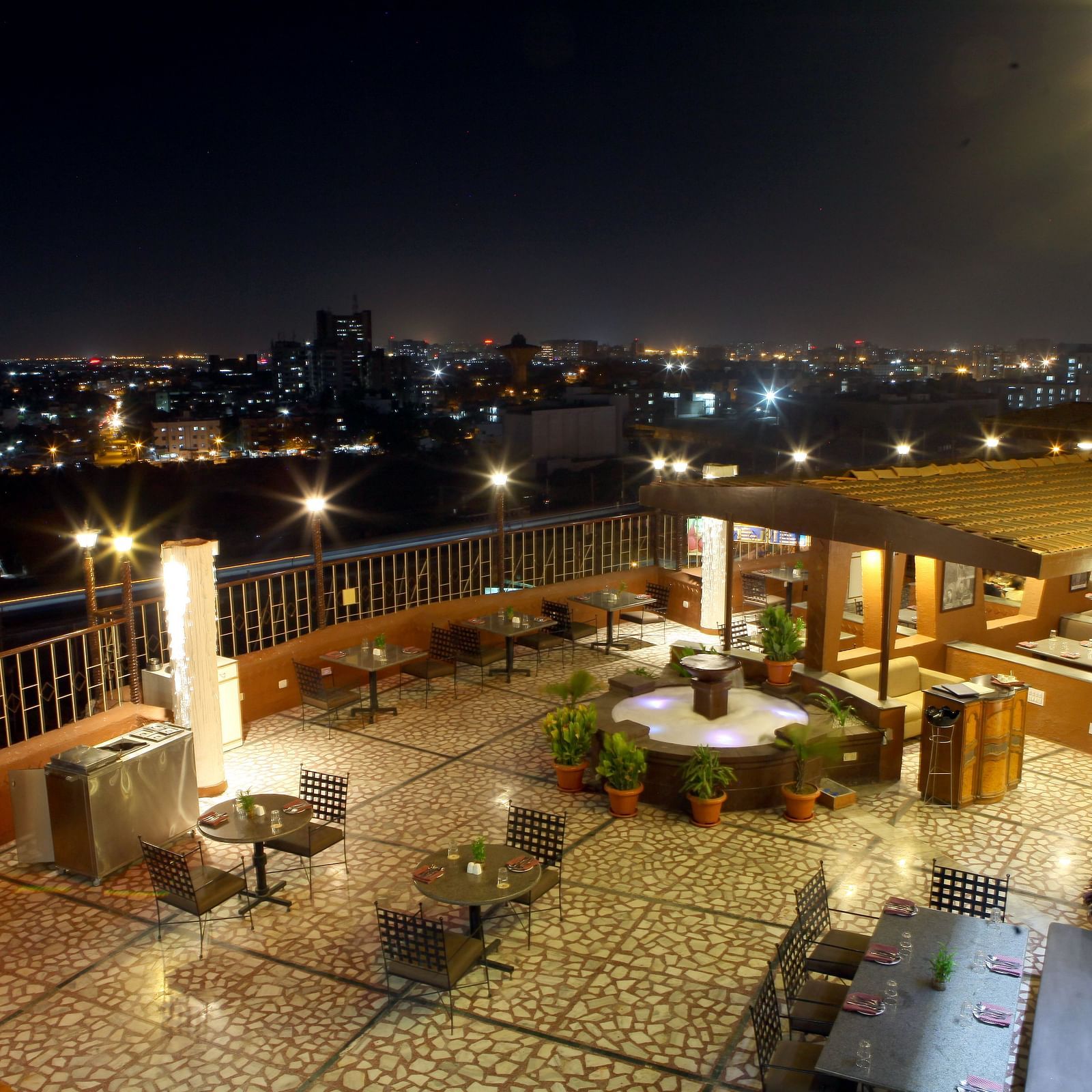 An outdoor seating area with city lights visible at night at Lords Plaza Surat.