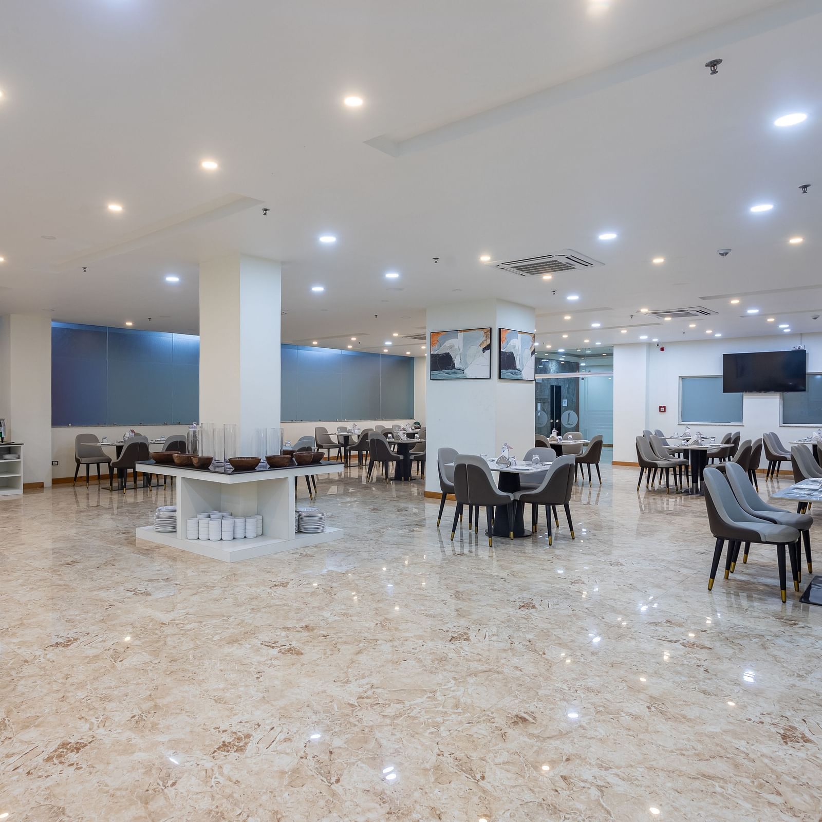 Corner view of the Blue Coriander Restaurant at Mandala Norling Lords Prime in Kathmandu with various seating arrangements, neatly placed cutlery and bright overhead lighting.