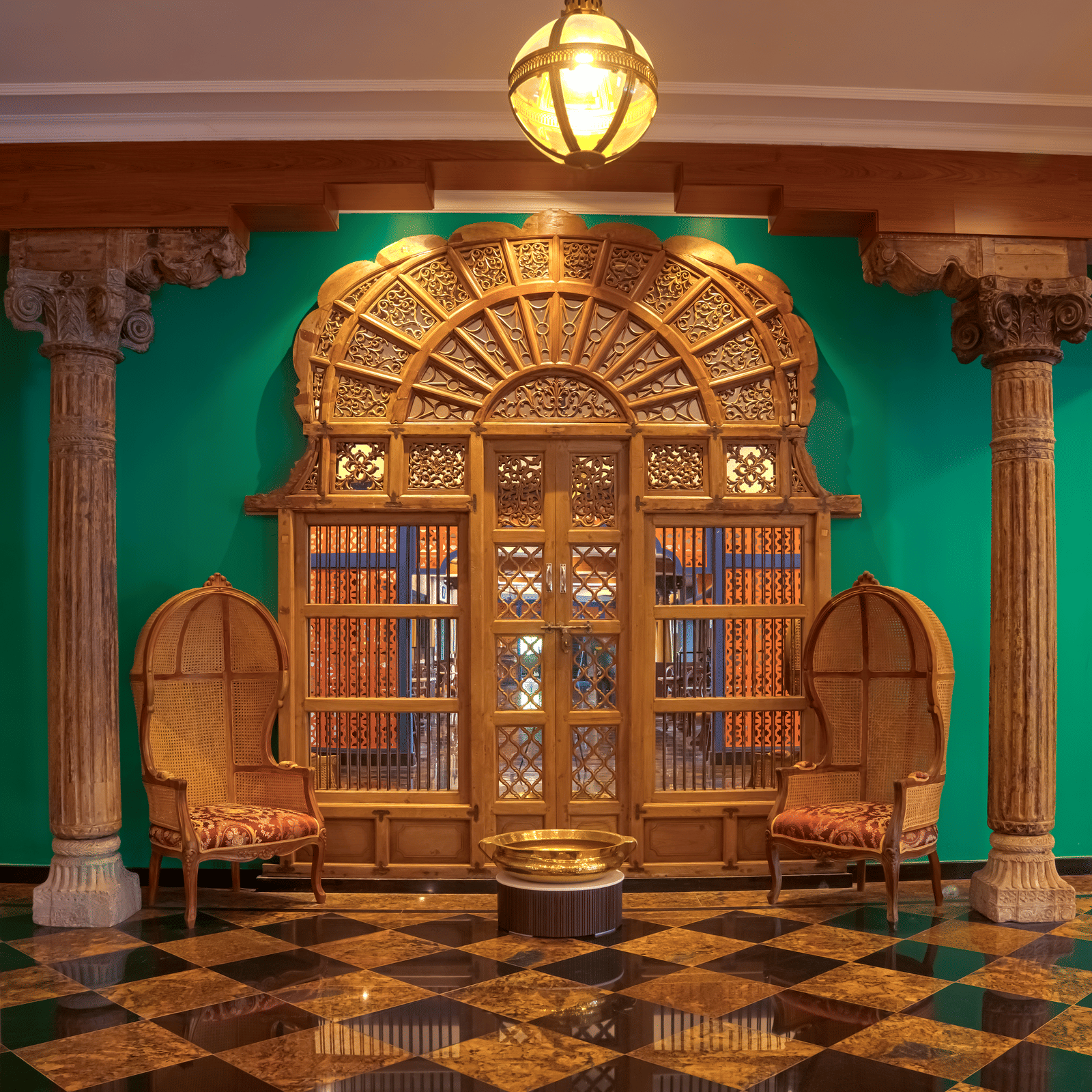 A richly designed corridor featuring carved wooden doors, ornamental seating, polished tiled flooring, green wall accents and overhead lantern lighting at MAYFAIR Bay Resort, Paradeep.