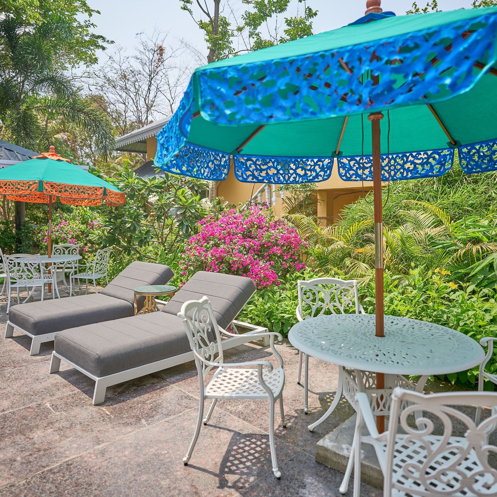Lounger chairs and an umbrella placed over the table, with plants and trees in the background at Mayfair Manor, Alibag
