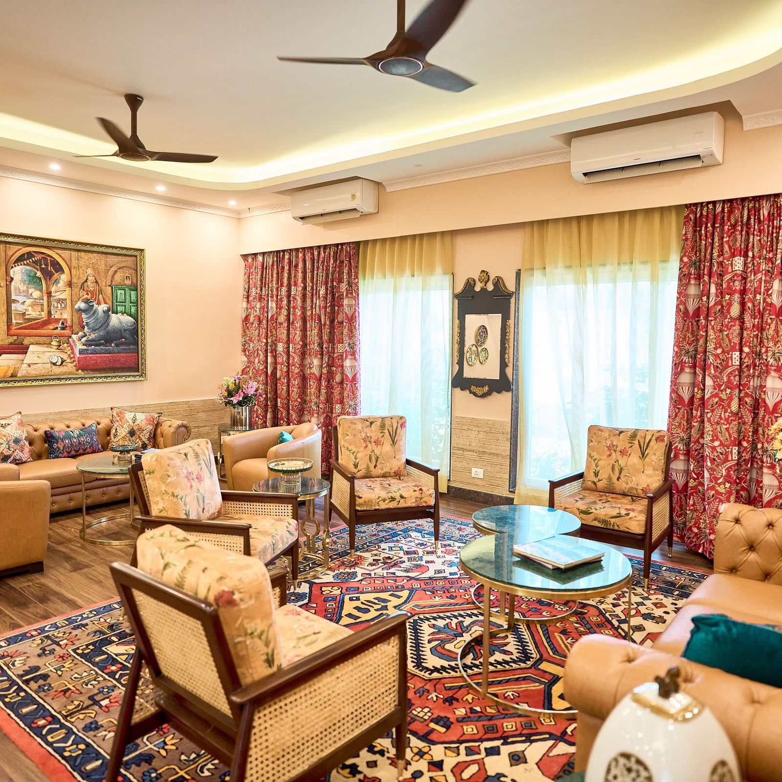  A seating area with plush furniture arranged around the table, curtains drawn to the side, and a wall-mounted painting at Mayfair Manor, Alibag