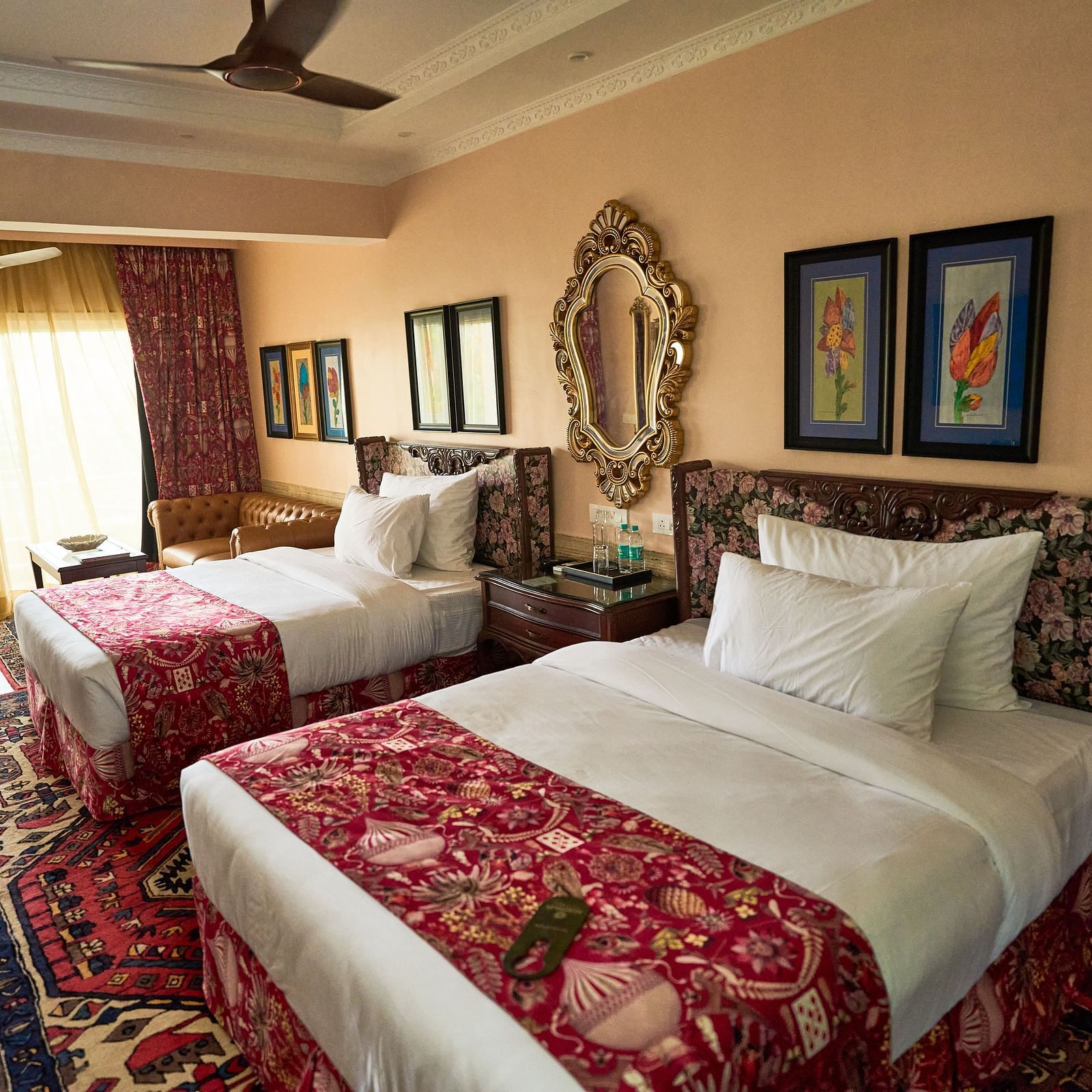 Side view of a spacious room featuring a double bed, wall-mounted frames for decoration, and windows elegantly covered with curtains at Mayfair Manor, Alibag