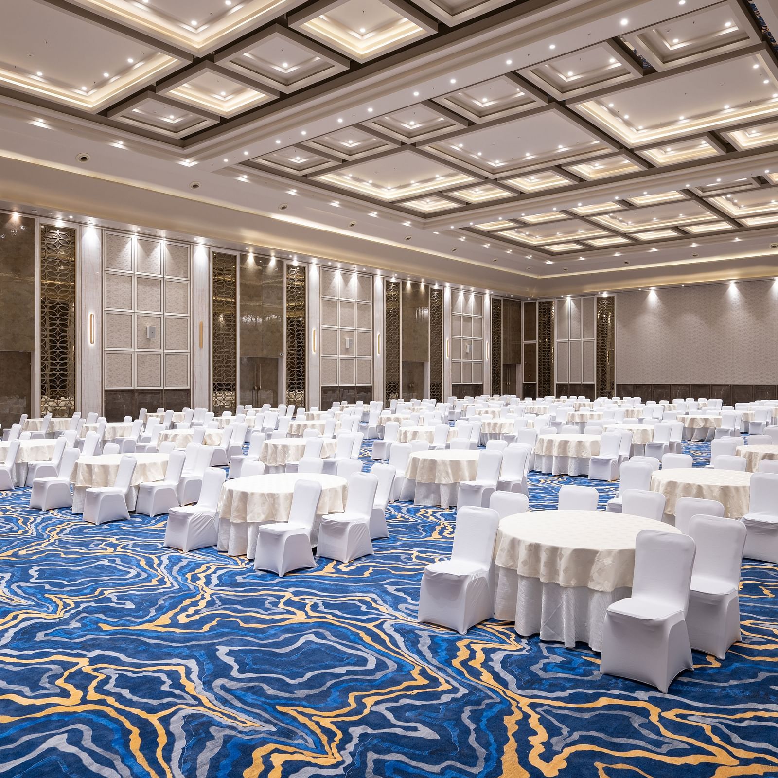 Banquet hall set up with round tables and white linen seating at Merlis Hotel, Coimbatore.