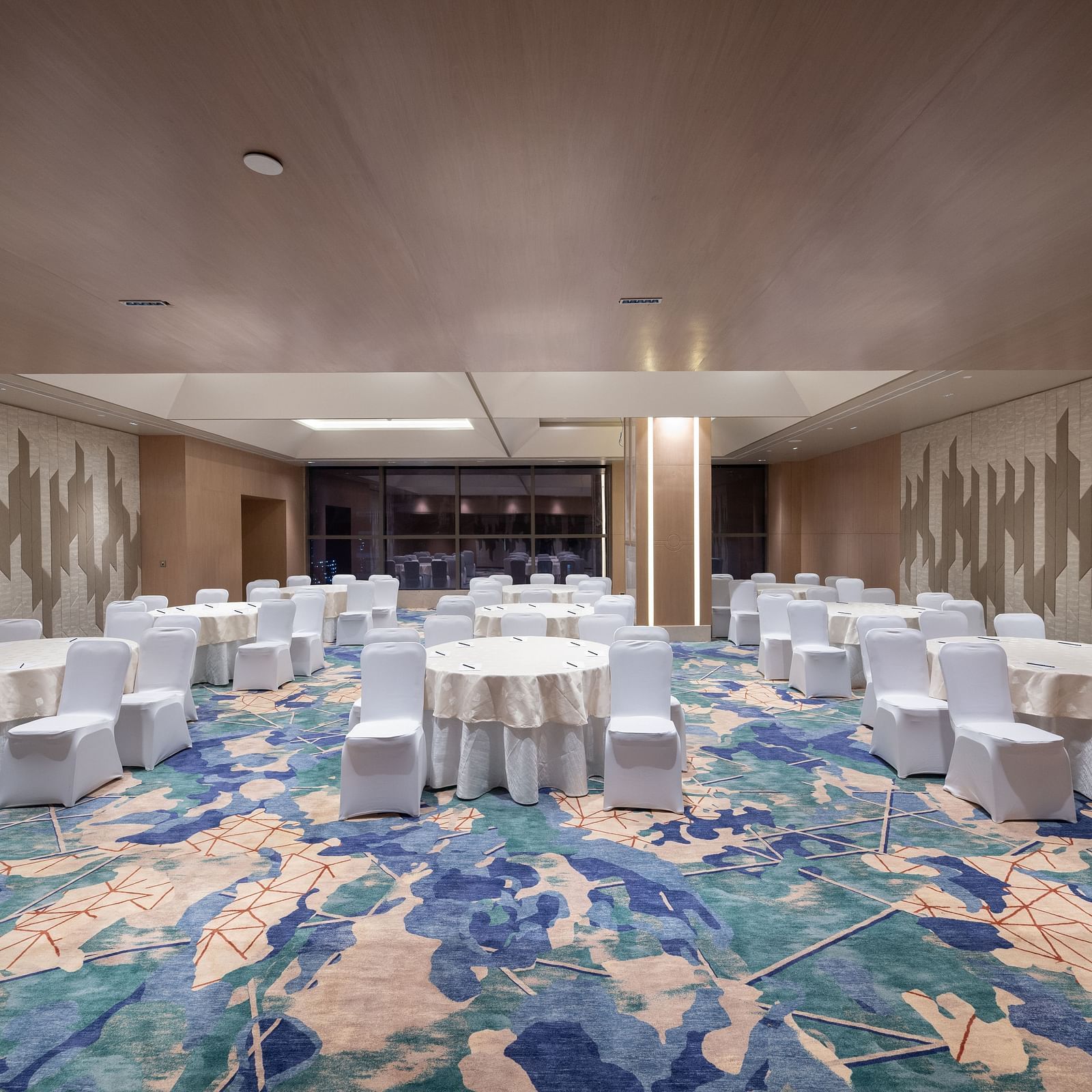 Round-table banquet setup in a spacious, well-lit function hall at Merlis Hotel, Coimbatore.