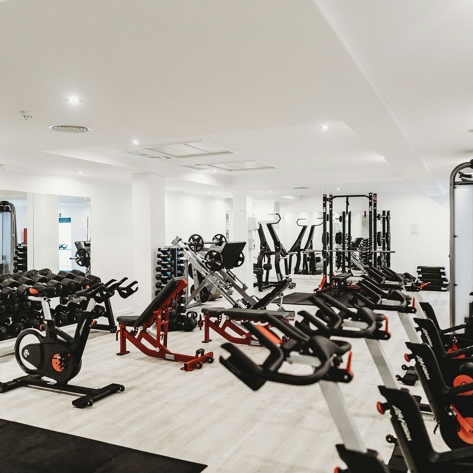 A brightly lit gym filled with various fitness equipment, including weights, exercise bikes, and resistance machines, indicating a comprehensive workout space.