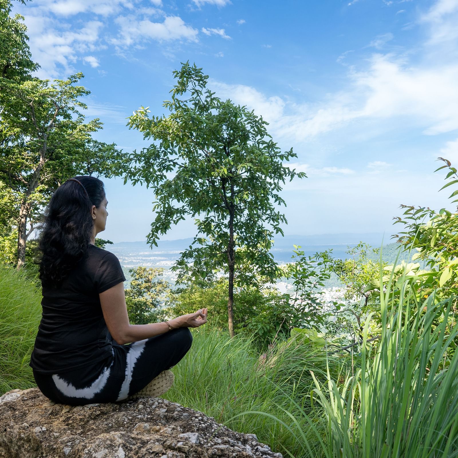 a lady sitting on a rock on top of the mountain with a view of the sky and meditating