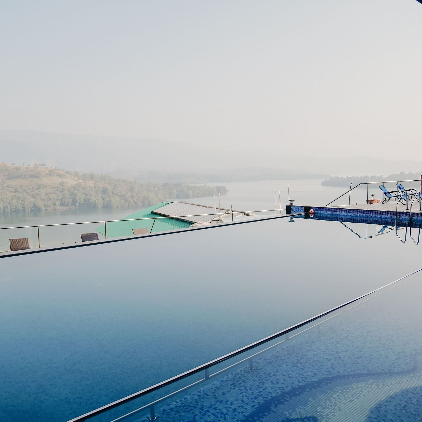 An image of the infinity waterfall swimming pool with a lake and mountain view in the background - Nisarga Lake Resort