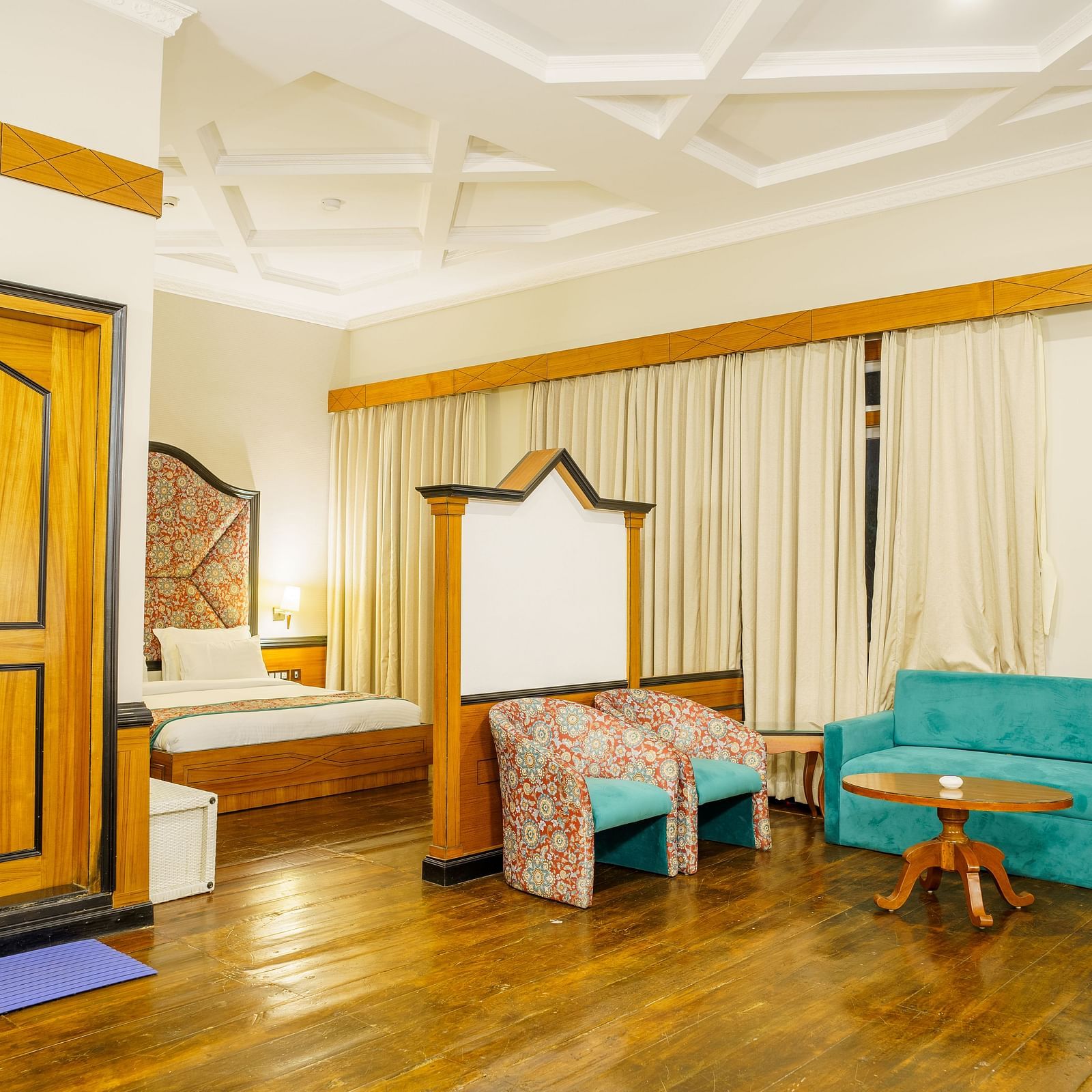A room at Orsino Spa Resort, furnished with a bed, a small sofa, a wooden table, and a wardrobe, with light-coloured walls and curtains.