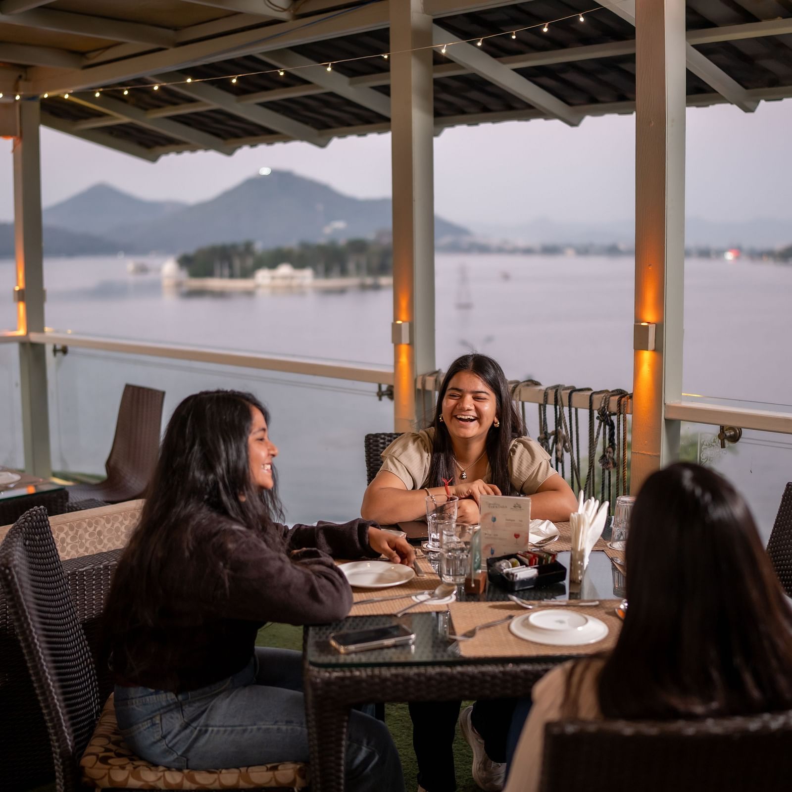 Guests enjoying a cheerful dinner at the rooftop restaurant of Panna Vilas Palace, overlooking the serene lake and surrounding hills at twilight.