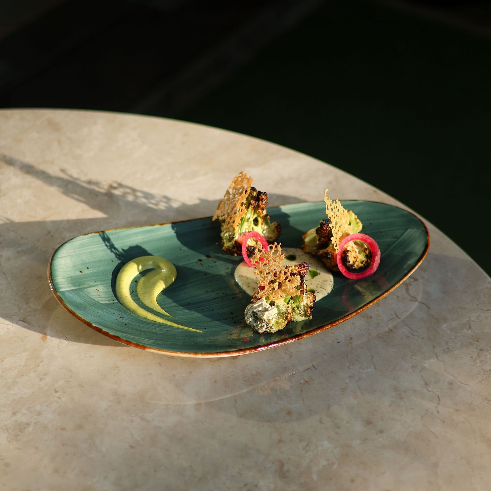 A gourmet vegetarian dish served at Panna Villas Palace, beautifully presented on a green ceramic plate with pickled onions, microgreens, cheese tuile, and artistic sauce swirls on a marble table.